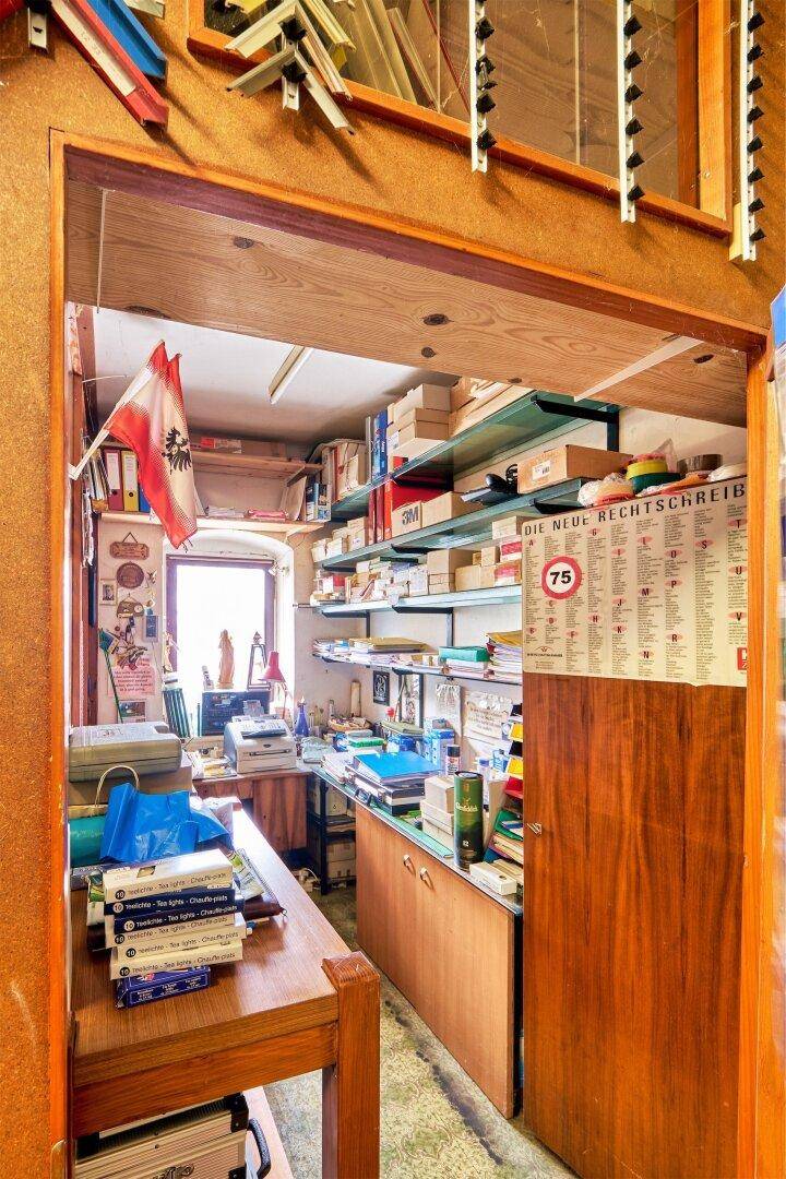 Kleines, vollgestelltes Büro mit Holzmöbeln, Regalen voller Akten und einem Fenster für natürliches Licht.