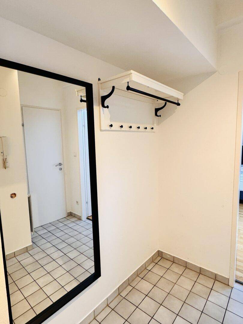 Heller Eingangsbereich mit Fliesenboden, großem Spiegel und einer praktischen Garderobe.