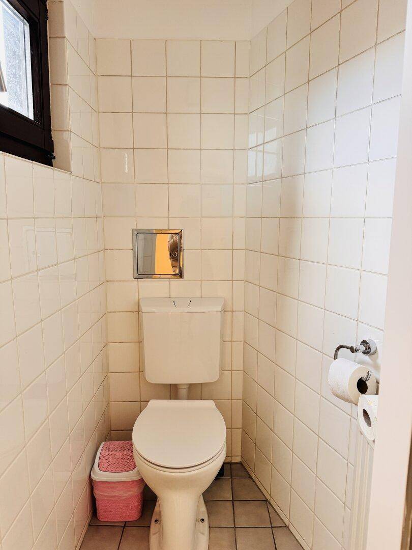 Separates WC mit Toilette, Fliesenboden und kleinem Fenster für natürliche Belüftung.