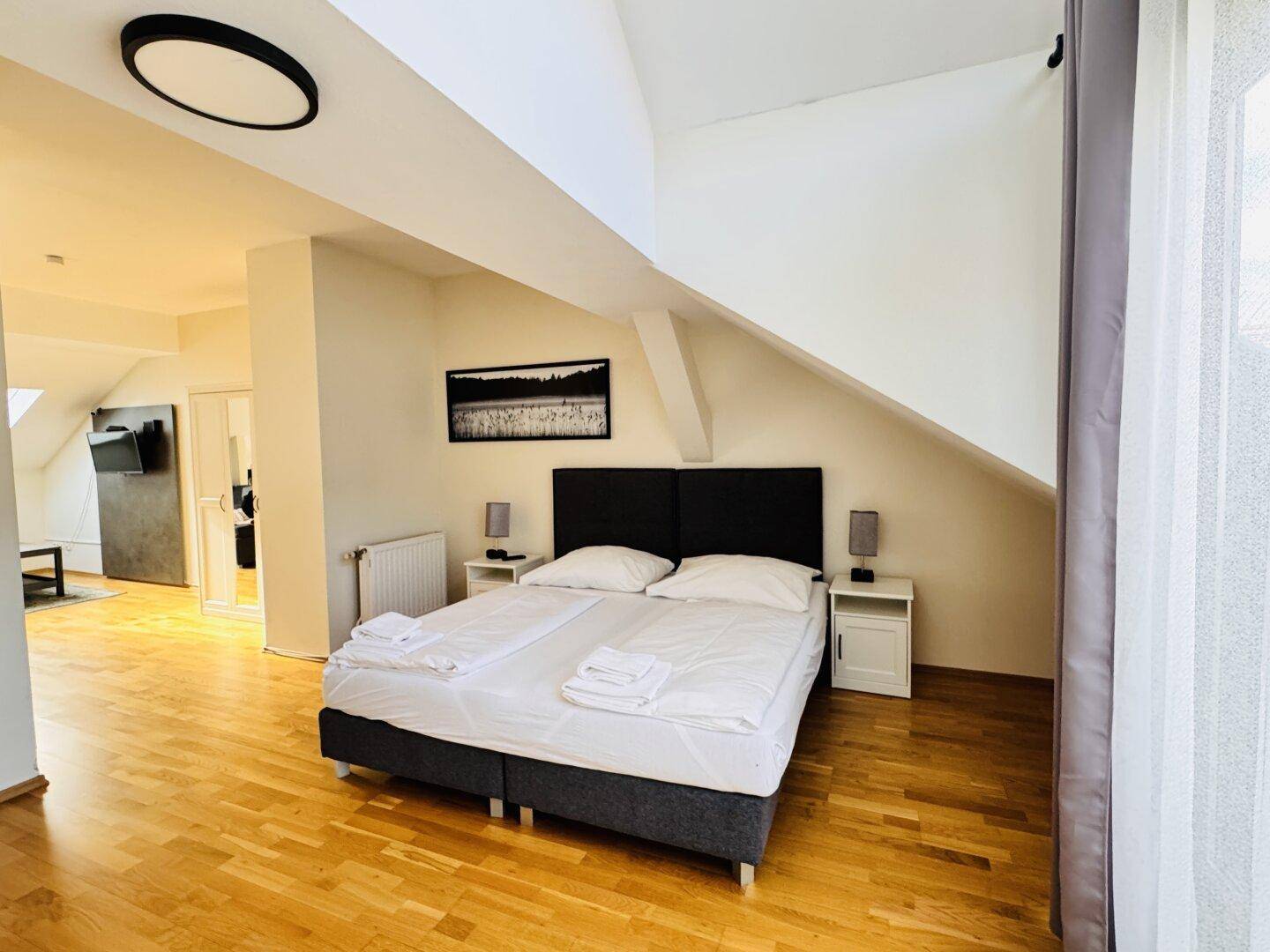 Gemütliches Schlafzimmer mit Holzboden, Doppelbett und Dachschrägen, offen zum Wohnbereich.