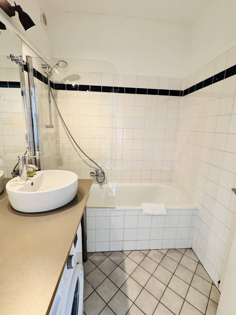 Badezimmer mit Badewanne, Dusche, Waschbecken und Waschmaschine, komplett gefliest.