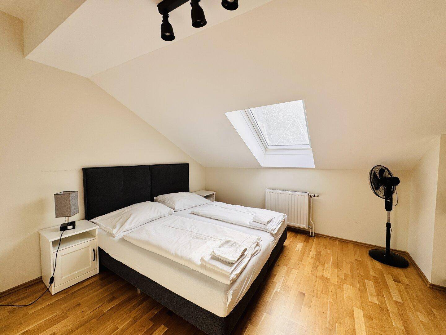 Helles Schlafzimmer im Dachgeschoss mit Holzboden, Doppelbett und einem praktischen Dachfenster.