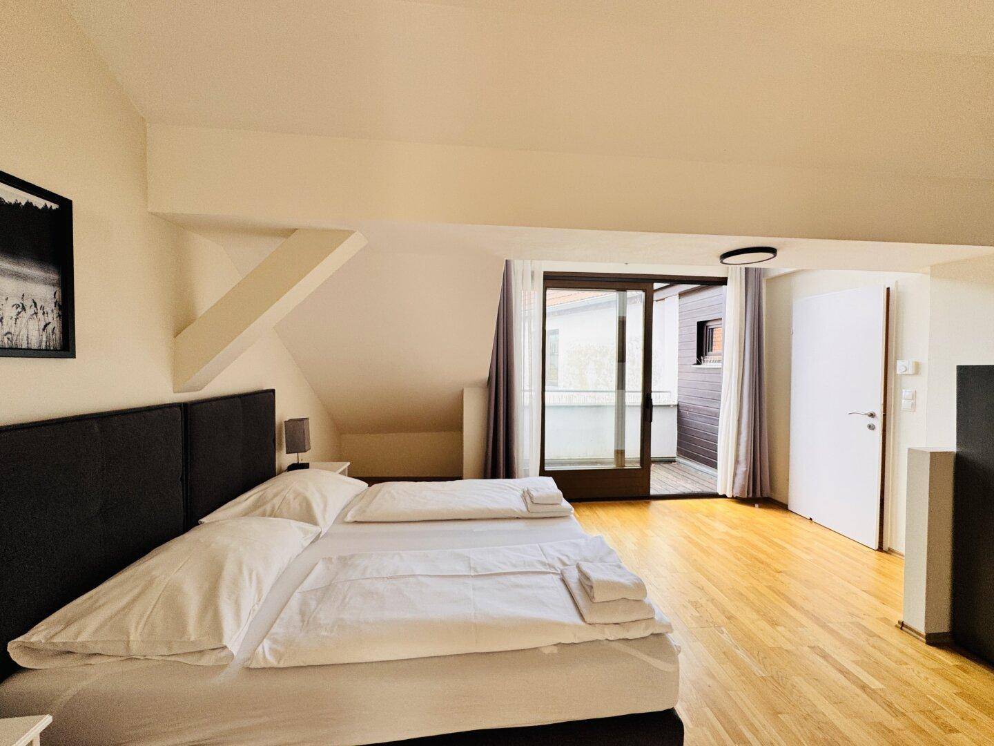 Schlafzimmer mit Doppelbett, Holzboden und direktem Zugang zu einem privaten Balkon.