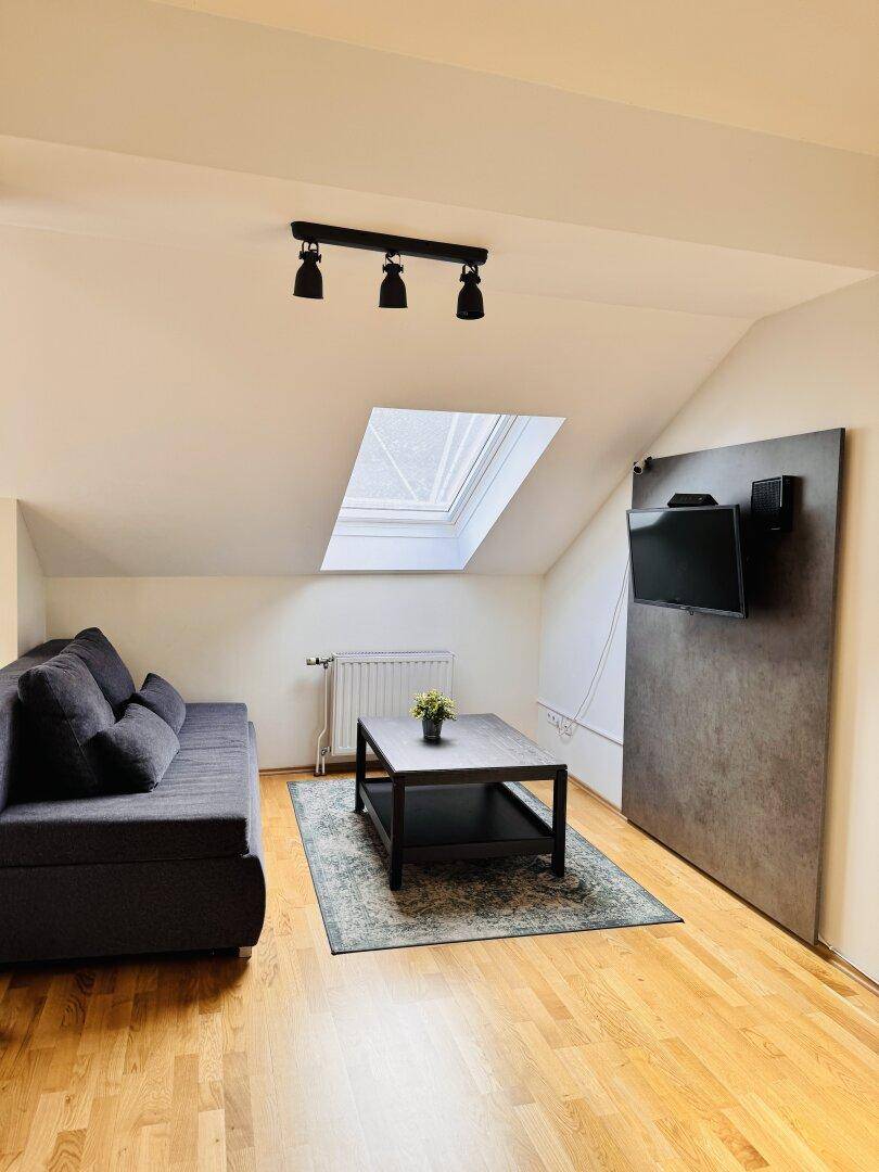 Gemütliches Wohnzimmer mit Sofa, Couchtisch, Fernseher und Dachfenster für viel Licht.