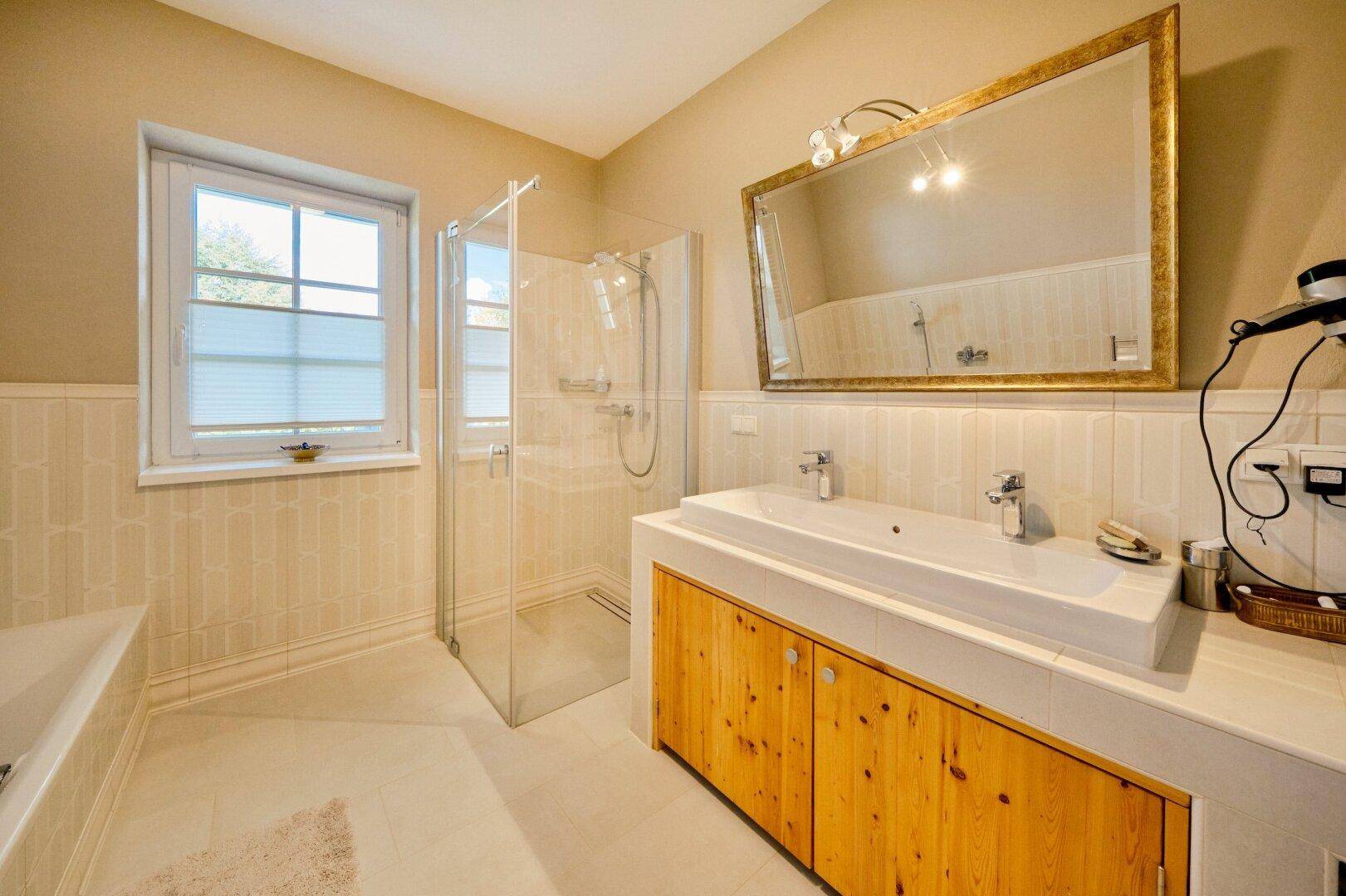 Helles Badezimmer mit Badewanne, Dusche, Doppelwaschbecken und Fenster.