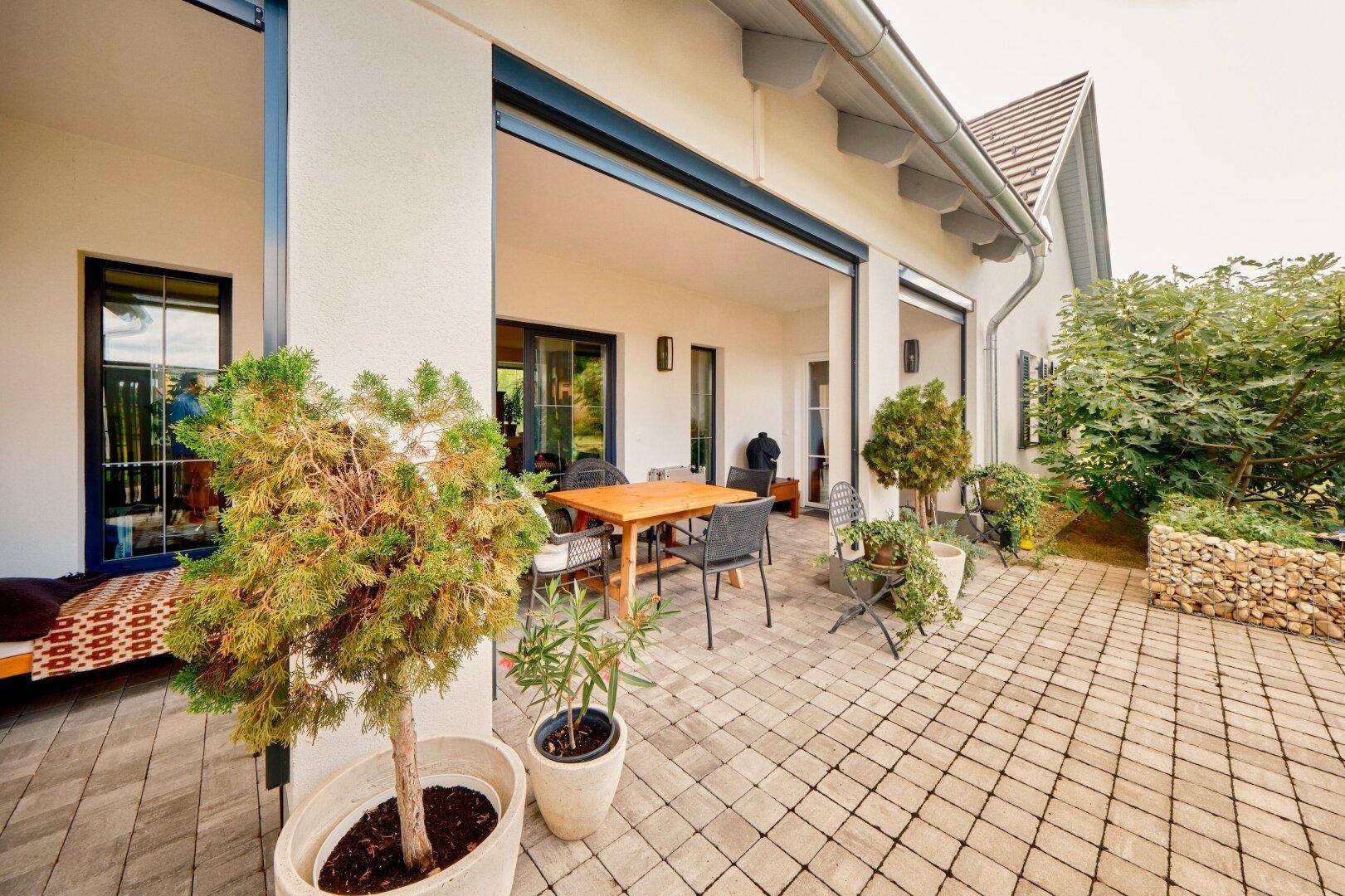 Geräumige gepflasterte Terrasse mit Gartenmöbeln und Topfpflanzen, angrenzend an das Wohnhaus.