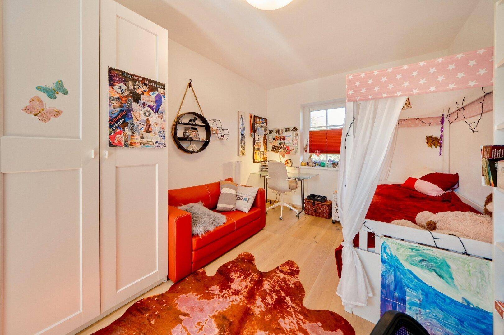 Farbenfrohes Kinderzimmer mit rotem Sofa, Himmelbett und Holzboden.