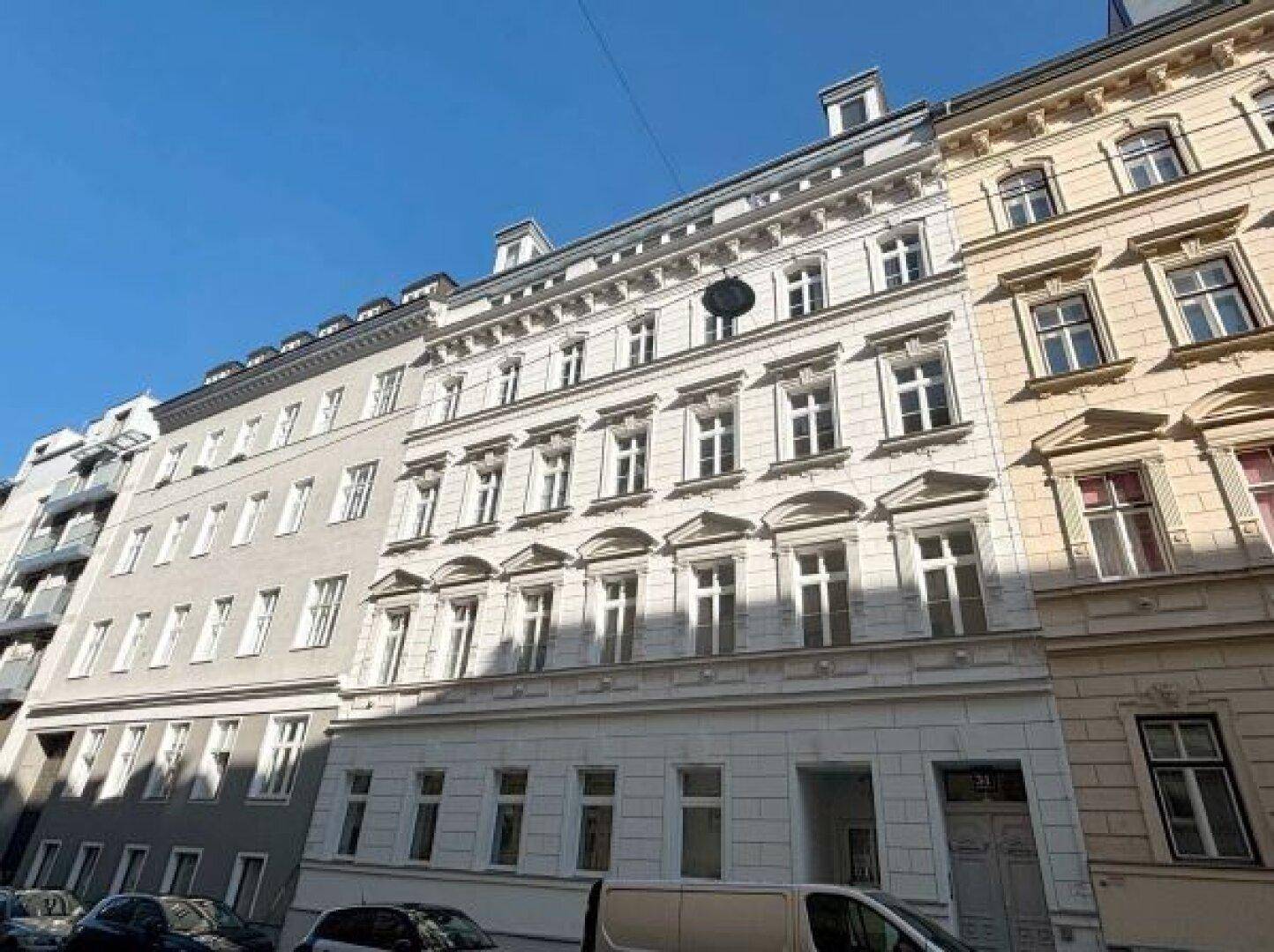 Klassische Altbaufassade mit vielen Fenstern und dekorativen Elementen unter blauem Himmel.