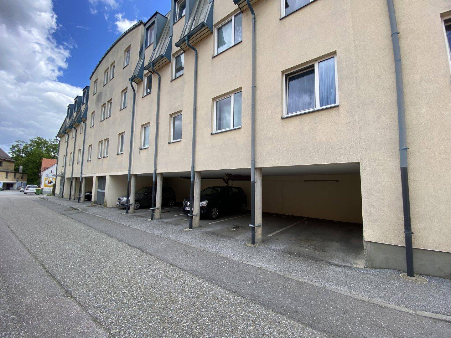 Seitenansicht des Apartmentgebäudes mit überdachten Parkplätzen im Erdgeschoss.