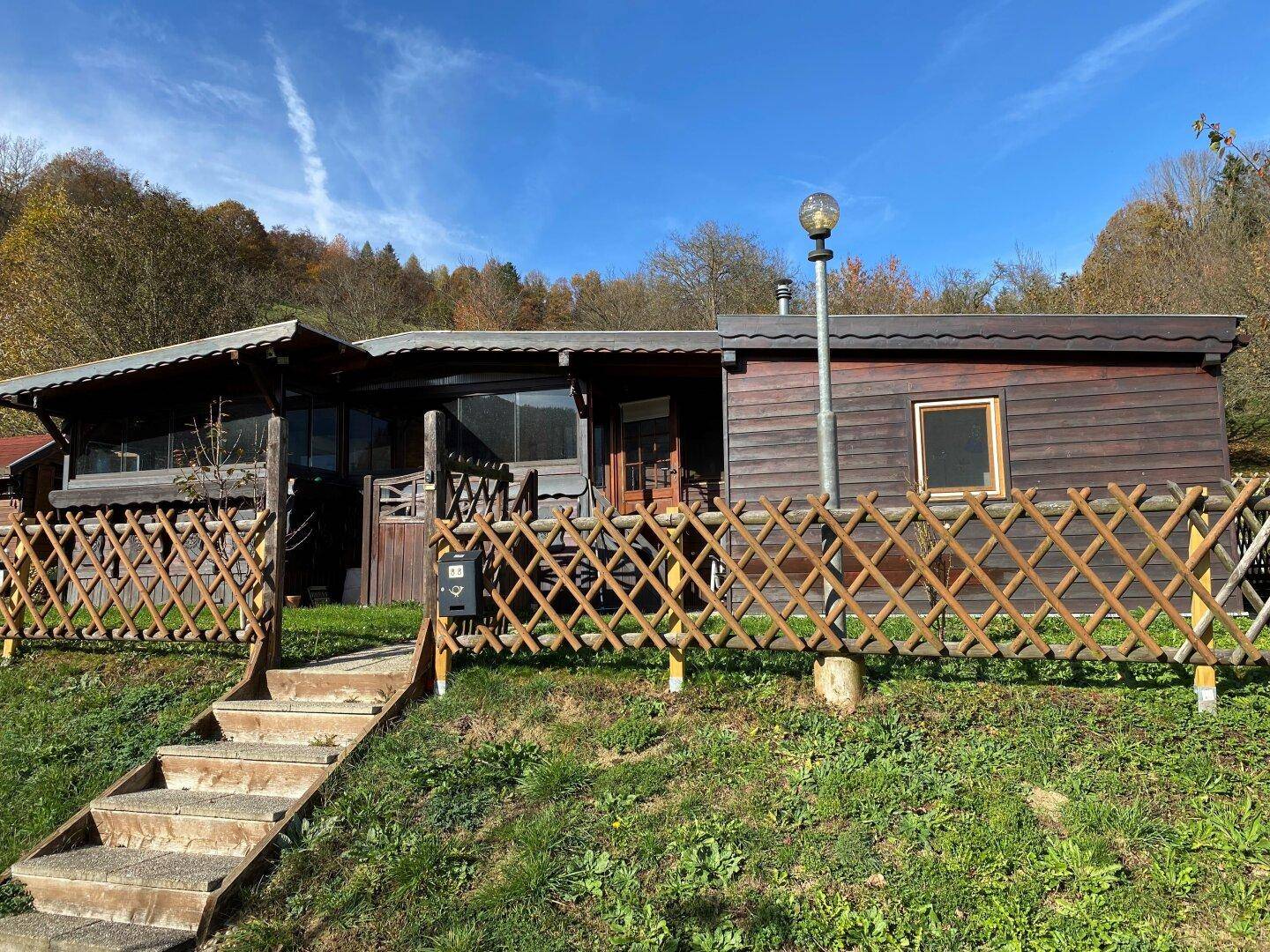 Rustikales Holzhaus mit Holzzaun und Treppe, eingebettet in die grüne Hügellandschaft.