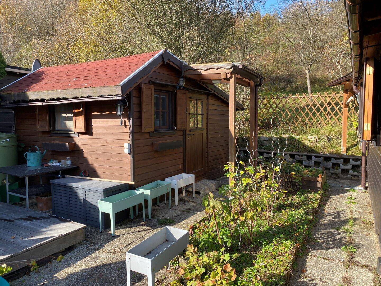 Kleines Holzhaus mit Gartenbereich, Hochbeeten und einer Terrasse im Freien.