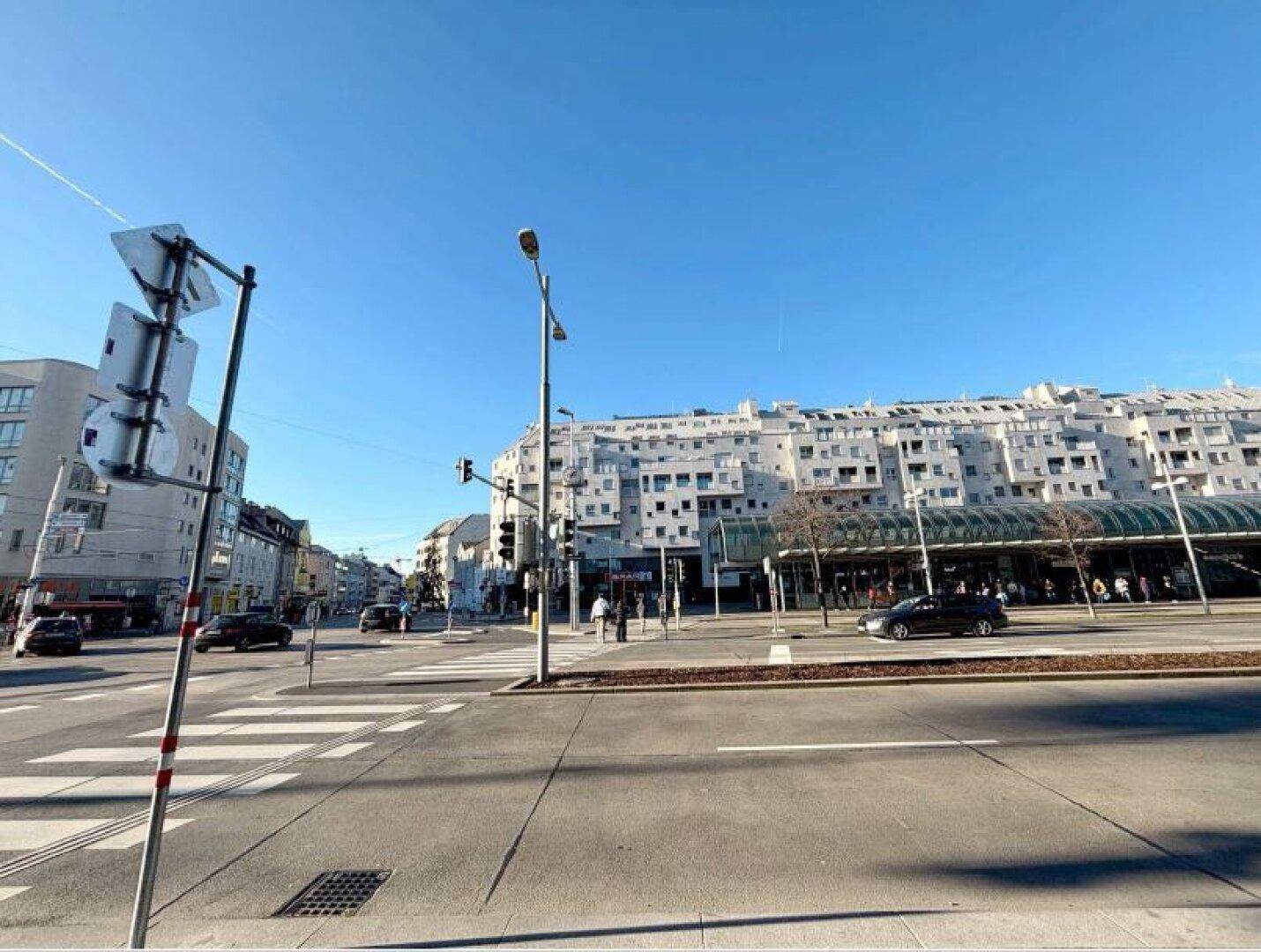 Weitläufige Straßenansicht mit einem großen, modernen Gebäude und klarem blauem Himmel.