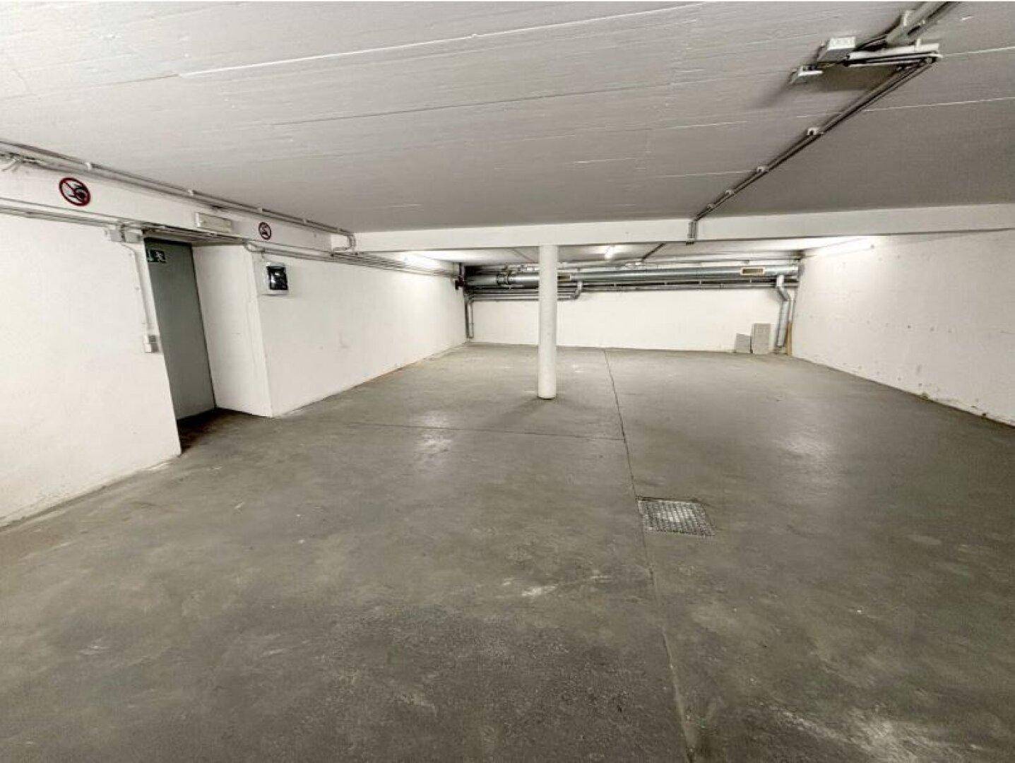Weitläufiger Garagenraum mit Betonboden, weißen Wänden und einer tragenden Säule in der Mitte.