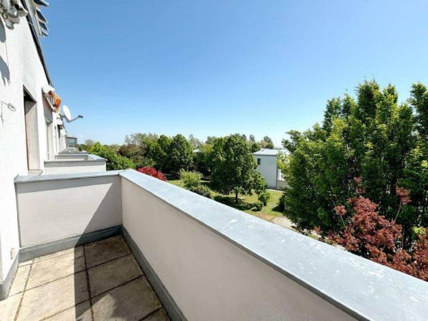 Balkon mit weitem Blick ins Grüne und auf umliegende Bäume, der Ruhe und Entspannung bietet.