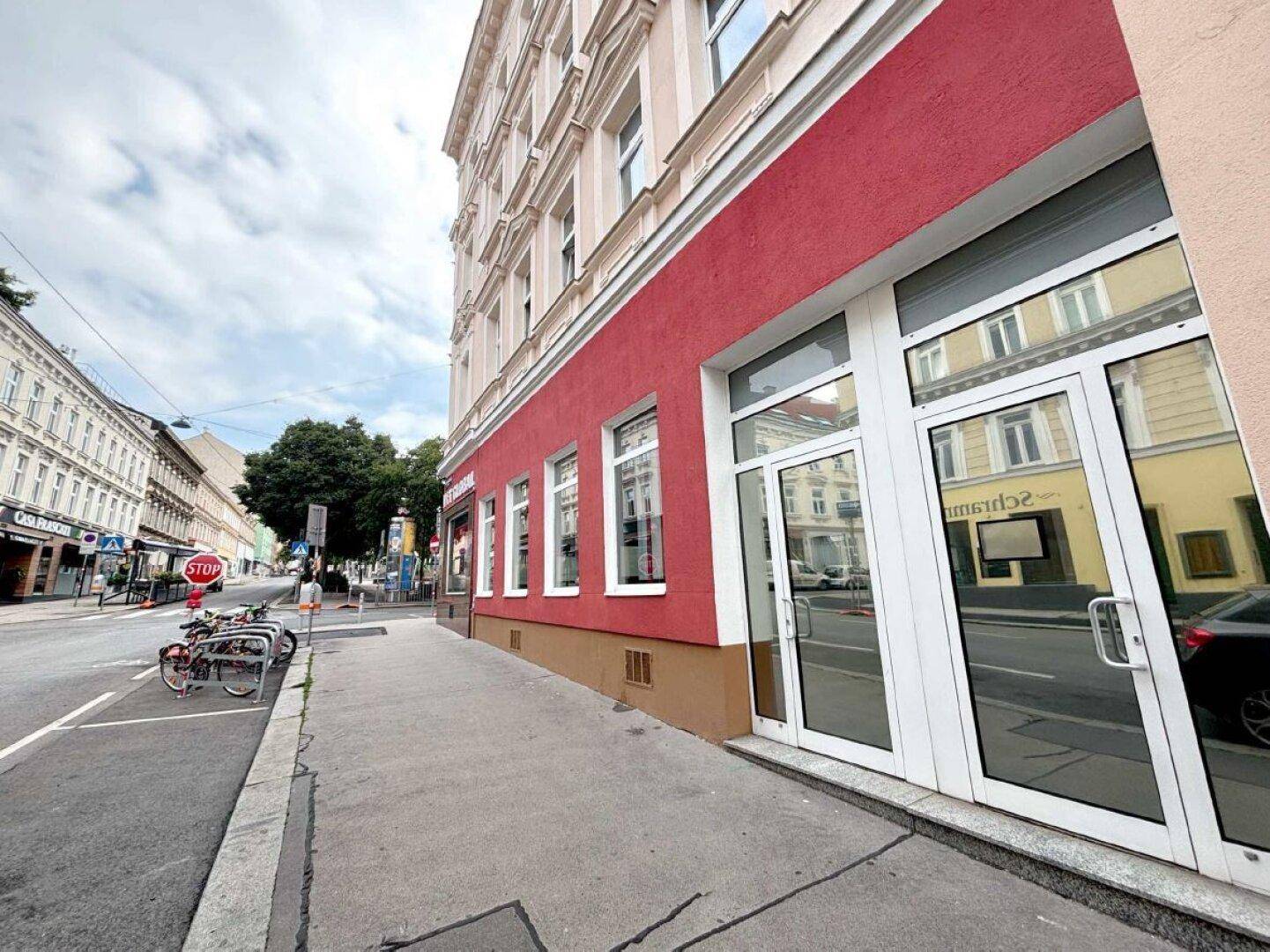 Rote Fassade eines Geschäftsgebäudes mit weißen Eingangstüren und Fenstern entlang einer Stadtstraße.