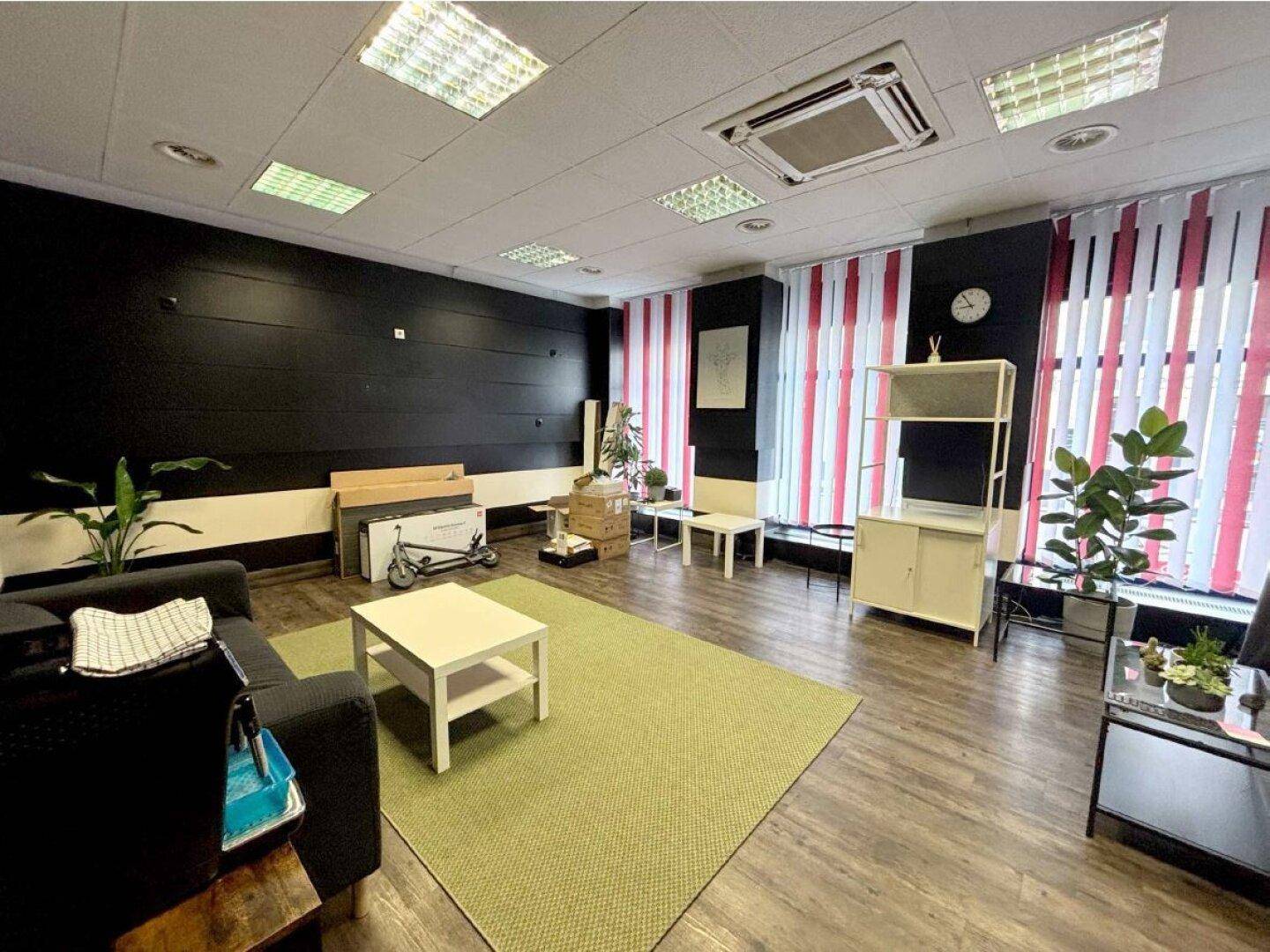 Weiterer Blick in den modernen Bürobereich mit Sofa, Couchtisch und Regalen, beleuchtet durch Deckenleuchten.