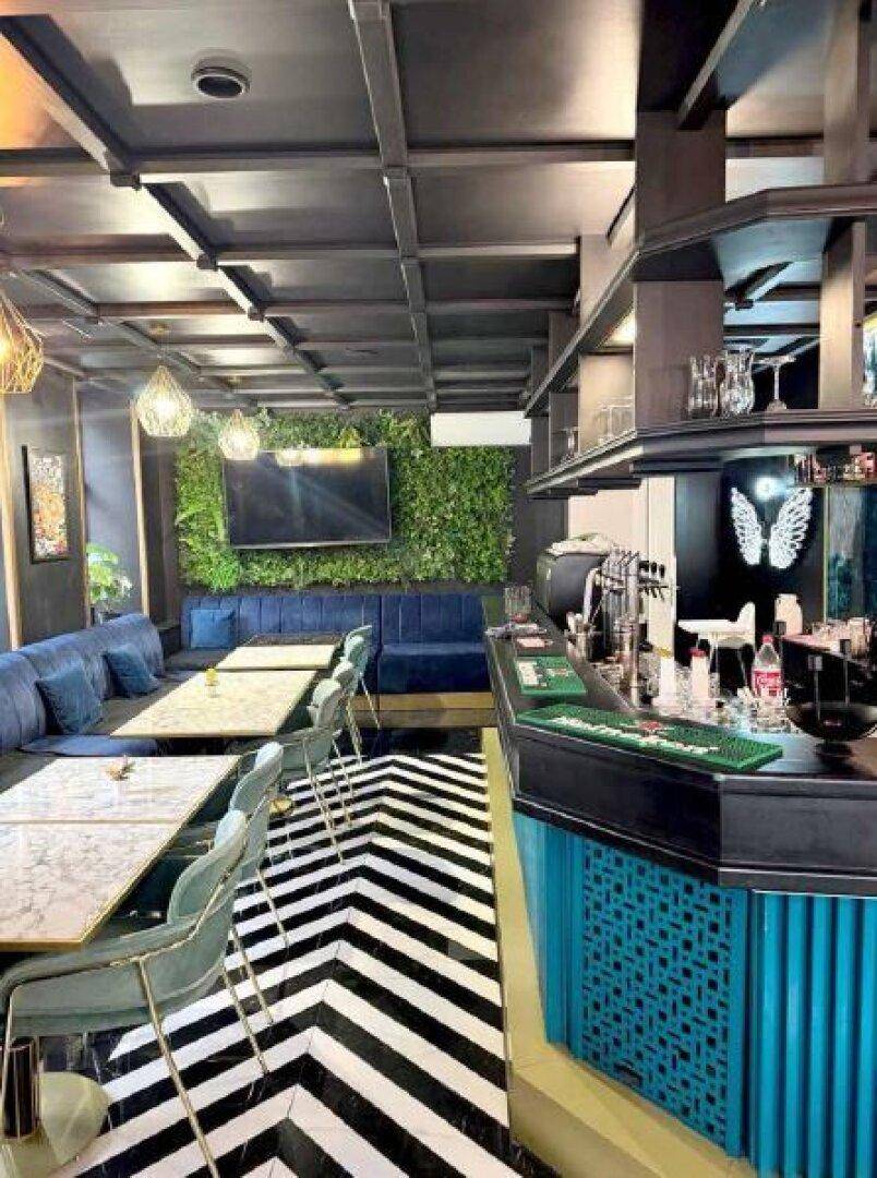 Stilvoller Restaurantbereich mit grüner Pflanzenwand, bequemen Sitzbänken und einer eleganten Bar.