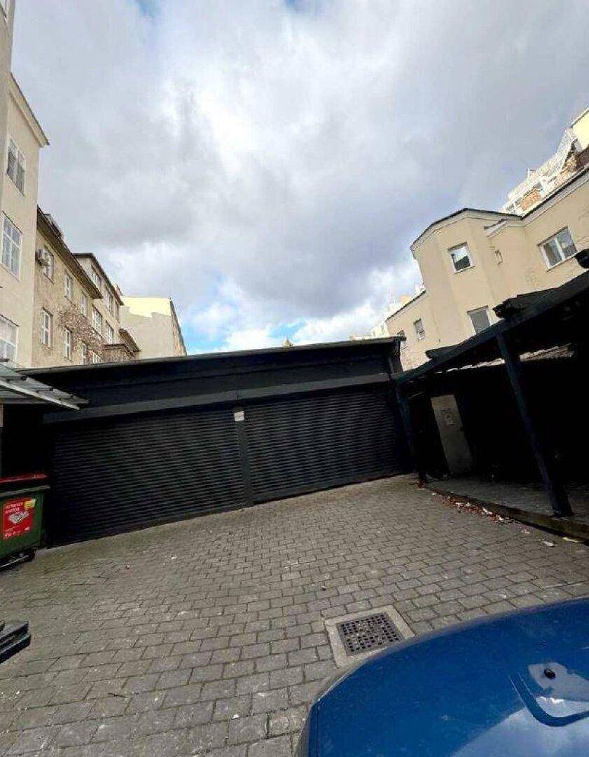 Außenparkplatz mit gepflastertem Boden und einer Garagenstruktur im Hintergrund unter bewölktem Himmel.