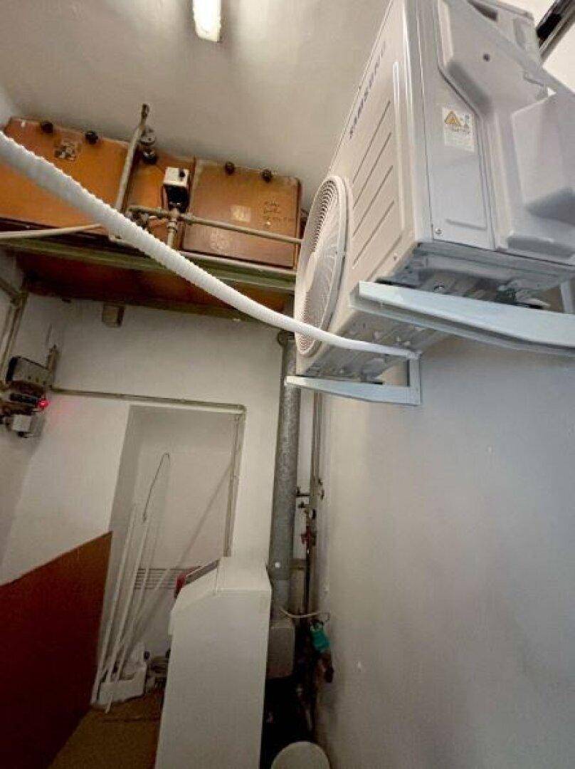 Technikraum mit einer Klimaanlage, Rohrleitungen und einem Warmwasserbereiter an der Wand.