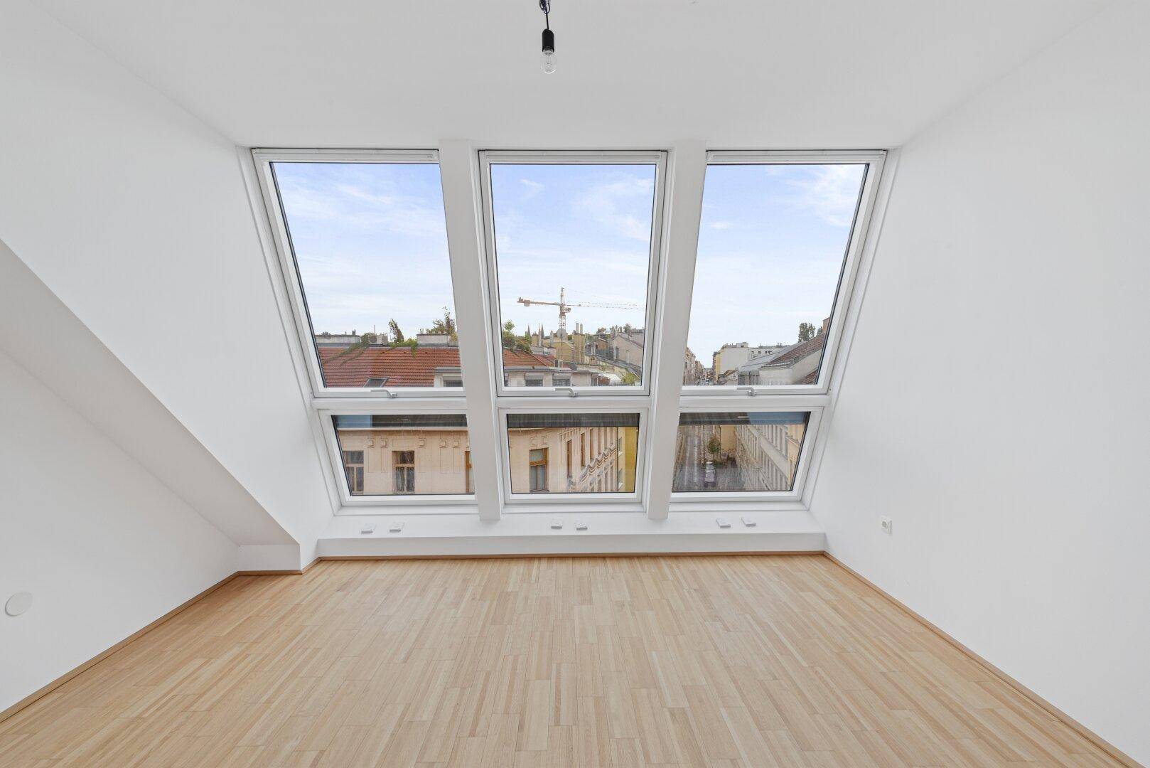 Geräumiger Wohnbereich mit Dachschrägen und großen Fenstern, die viel Tageslicht hereinlassen.