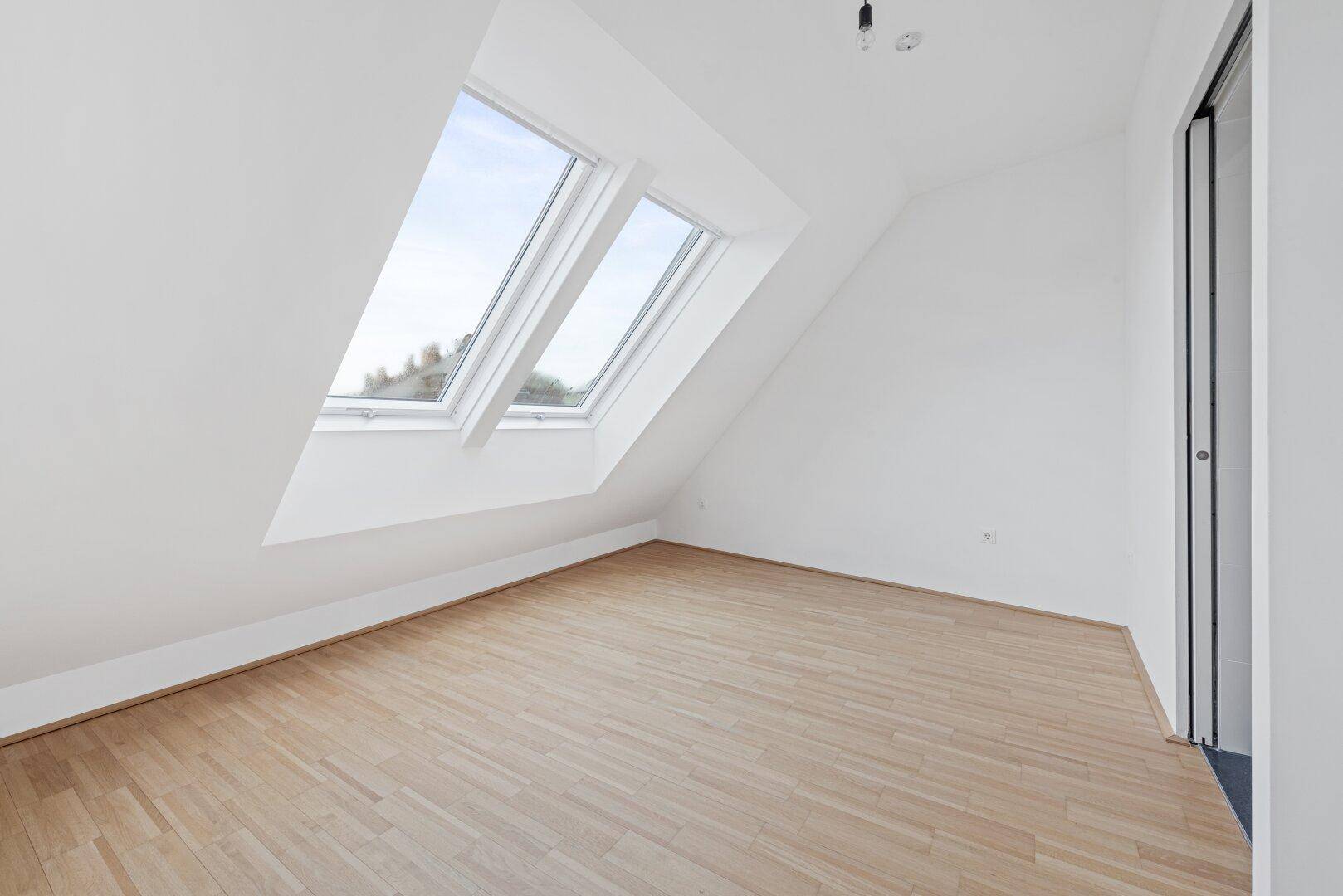 Schlafzimmer im Dachgeschoss mit schrägen Wänden und zwei Dachfenstern.