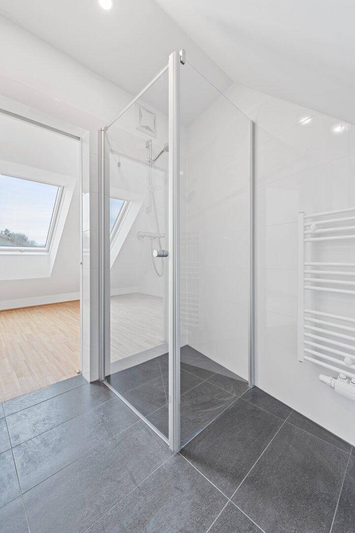 Modernes Badezimmer mit Glasdusche, Handtuchheizkörper und Fliesenboden.