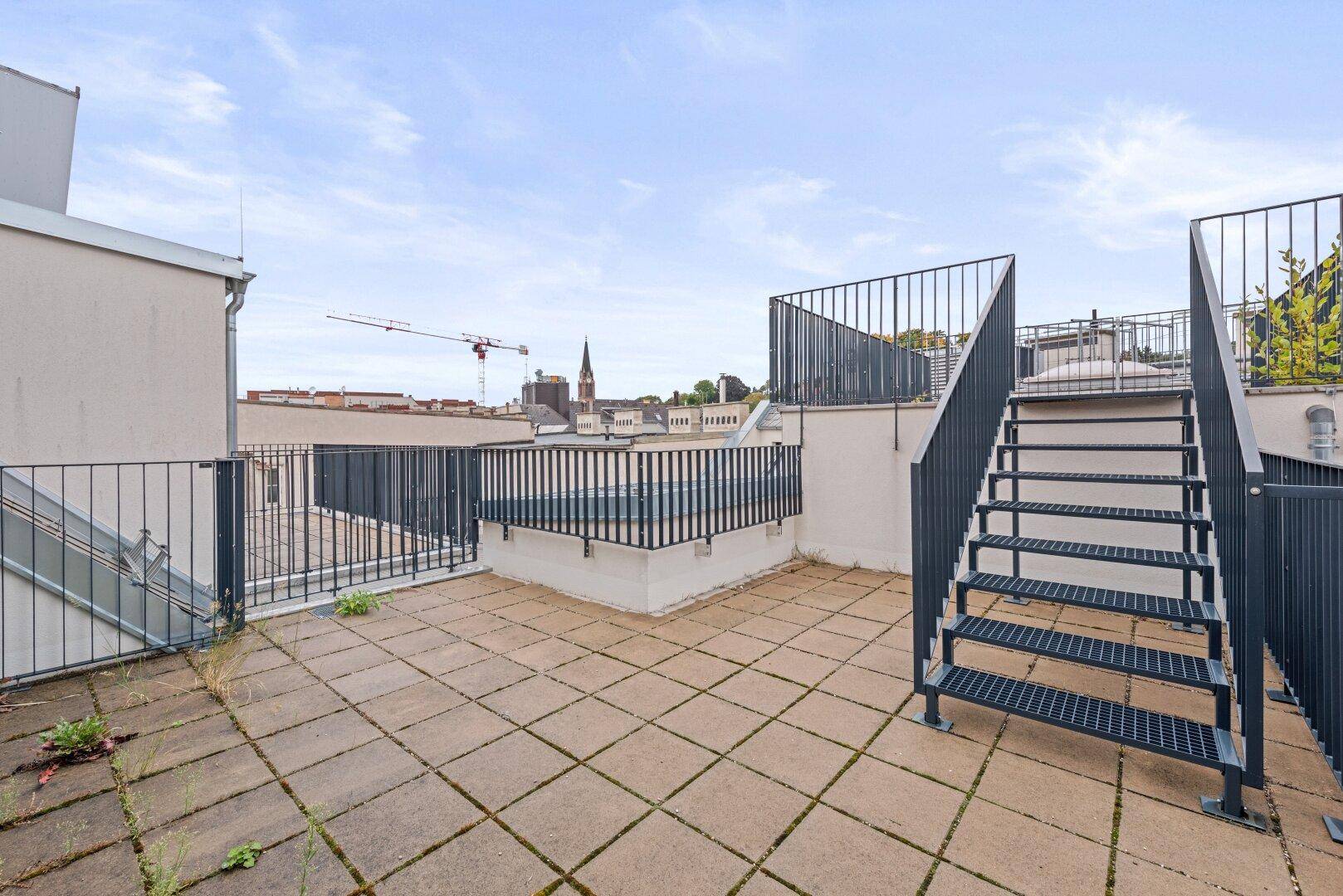 Weitläufige Dachterrasse mit Metallgeländer und Treppe zu einer weiteren Ebene.