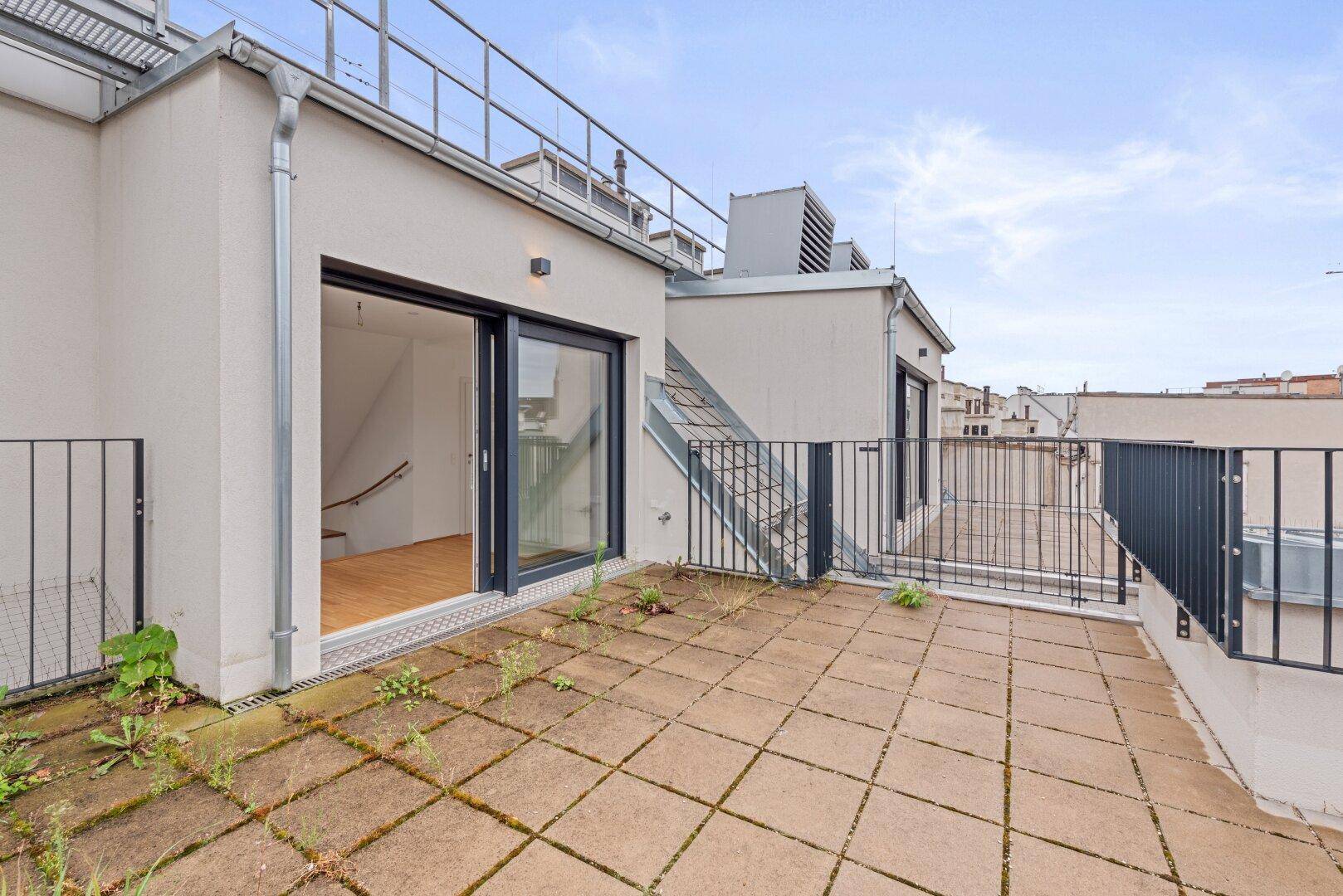 Große Dachterrasse mit Fliesenboden und Blick auf die umliegenden Gebäude.
