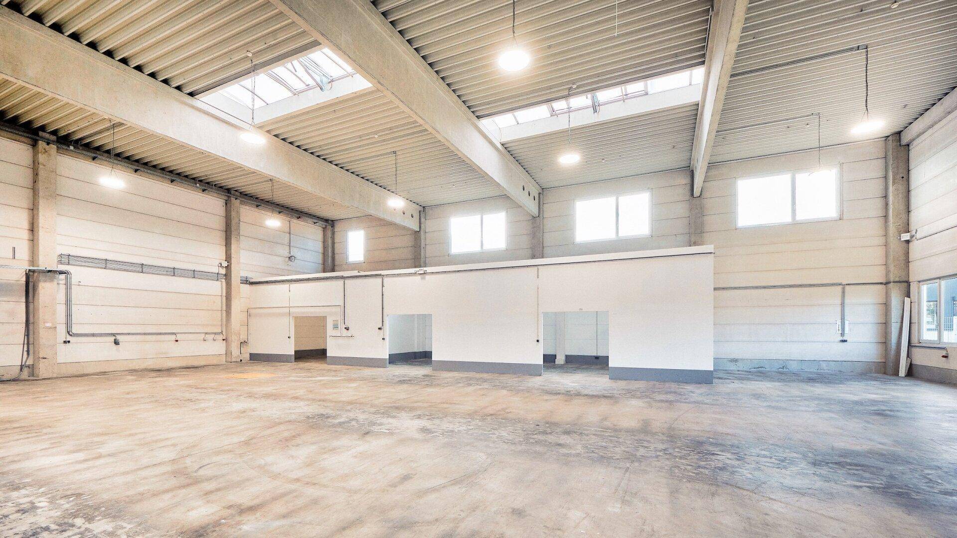 Weitläufige Lagerhalle mit Betonboden, Oberlichtern und mehreren Zugängen zu weiteren Räumen.