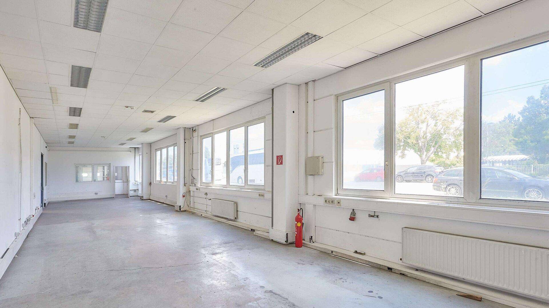 Langer Büroraum mit vielen Fenstern, Heizkörpern und einem Feuerlöscher an der Wand.