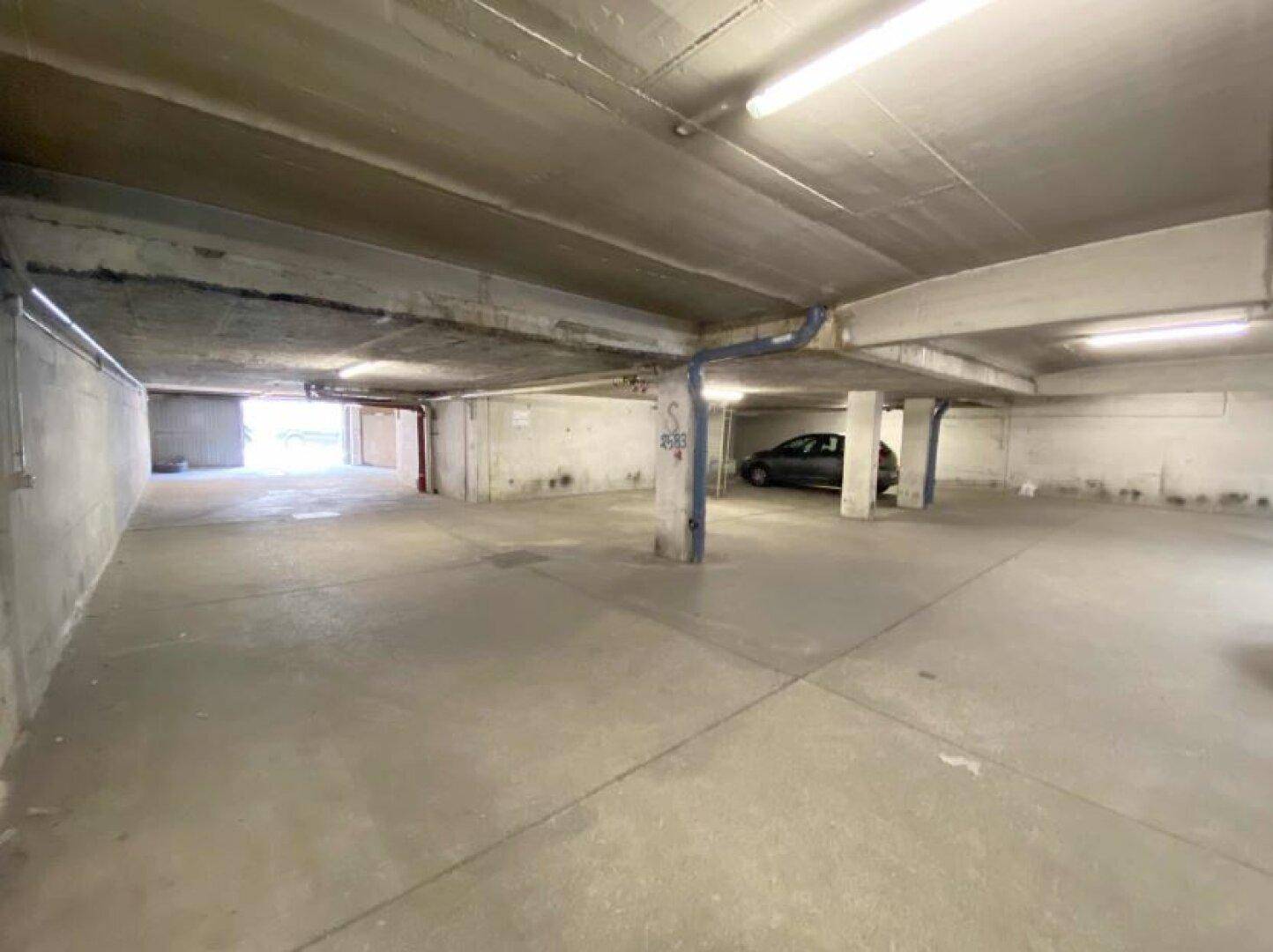 Weitläufige Tiefgarage mit Betonpfeilern und hellen Leuchtstoffröhren, ein Fahrzeug ist im Hintergrund sichtbar.