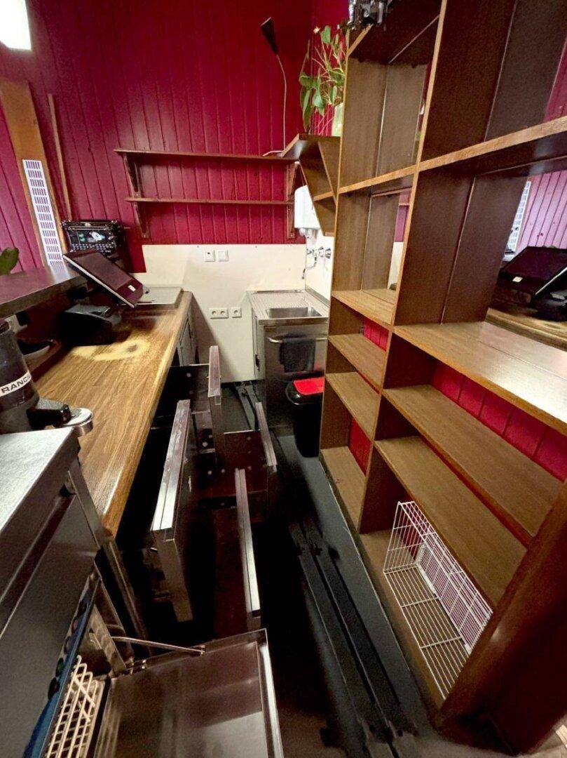 Schmaler Servicebereich hinter der Bar mit Spüle, Arbeitsflächen und Regalen für Getränke und Utensilien.