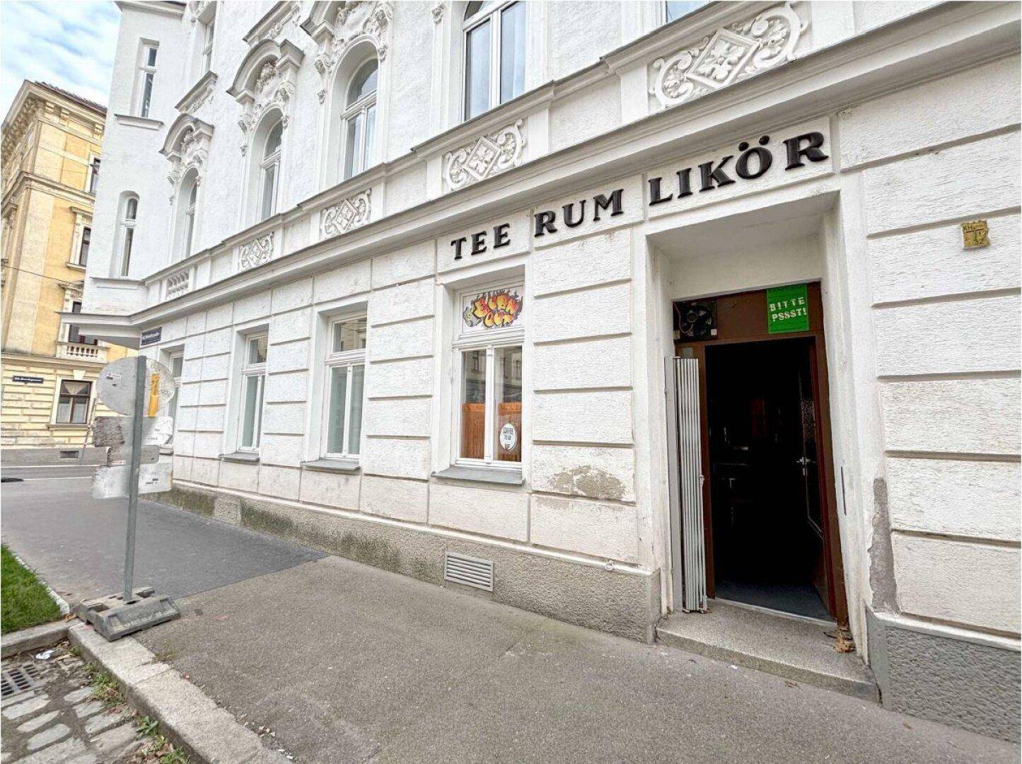 Historische weiße Fassade eines Gebäudes mit großen Fenstern und einem Geschäftseingang auf Straßenniveau.