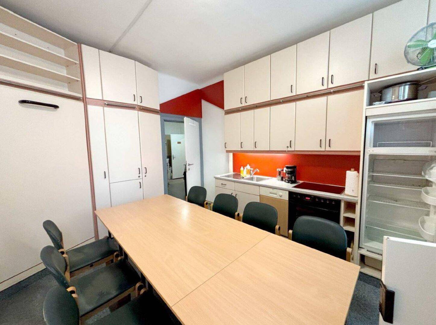 Geräumiger Büro- oder Pausenraum mit langer Tafel, Einbauschränken und integrierter Küchenzeile.