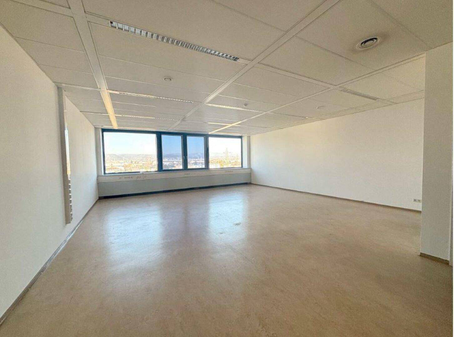 Helles und leeres Büro mit großen Fenstern und einer Deckenkonstruktion, ideal für gewerbliche Nutzung.