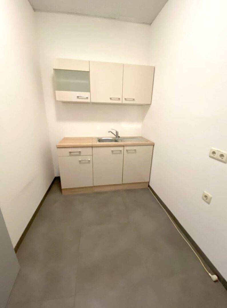 Kleine Küchenzeile mit Spüle, Unterschränken und Hängeschränken in einem Büroraum.