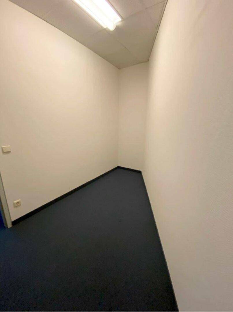 Kleiner, leerer Büroraum mit blauem Teppichboden und weißen Wänden.