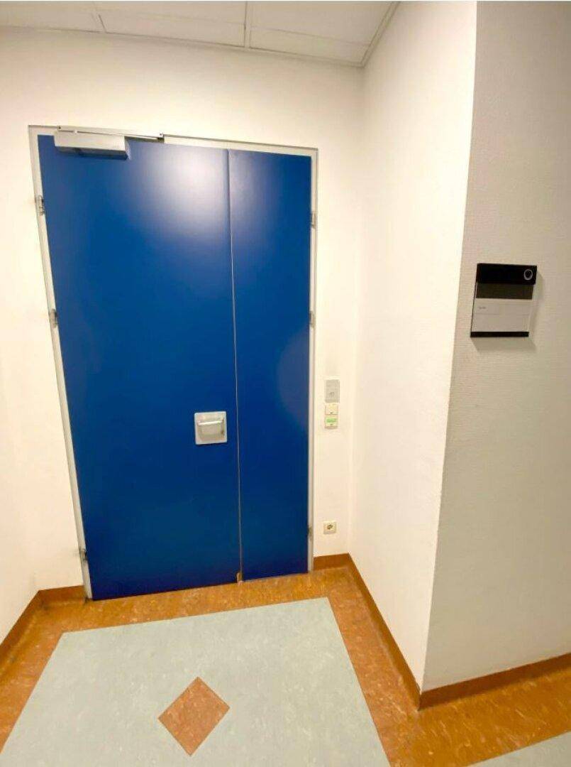Große blaue Doppeltür in einem Flur mit gemustertem Bodenbelag und weißen Wänden.