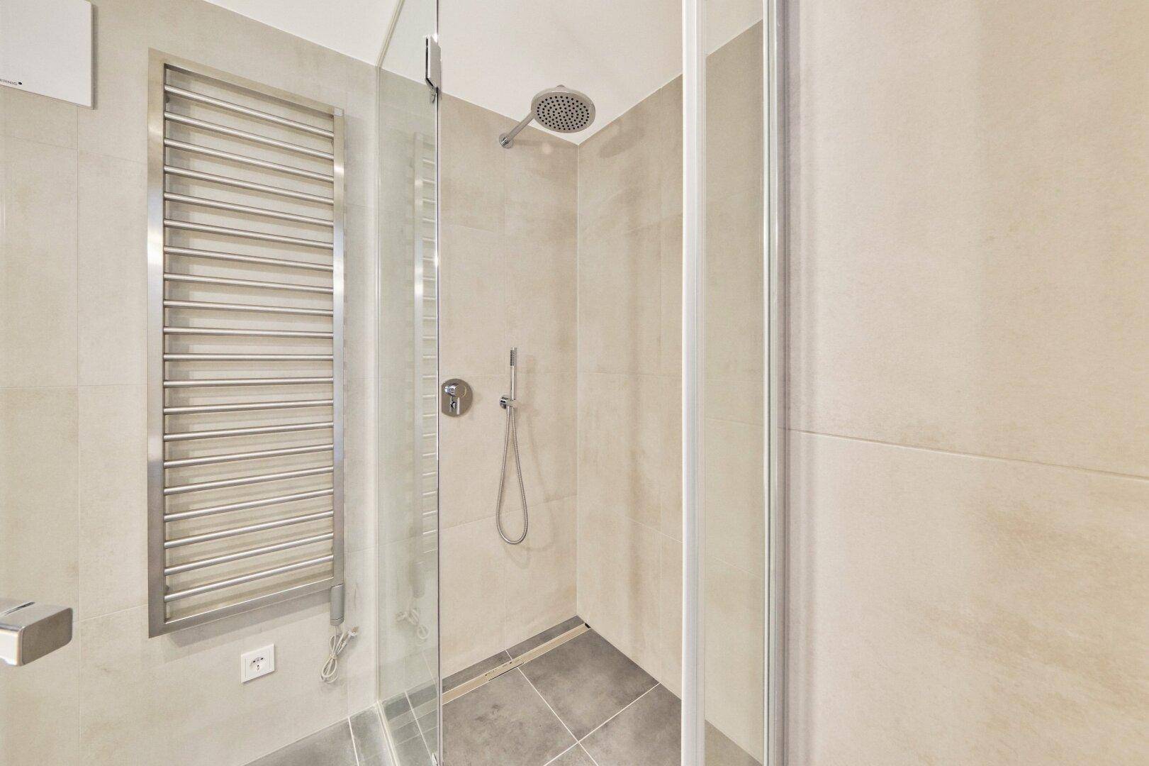 Duschbereich im modernen Badezimmer mit Regendusche und praktischem Handtuchheizkörper an der Wand.