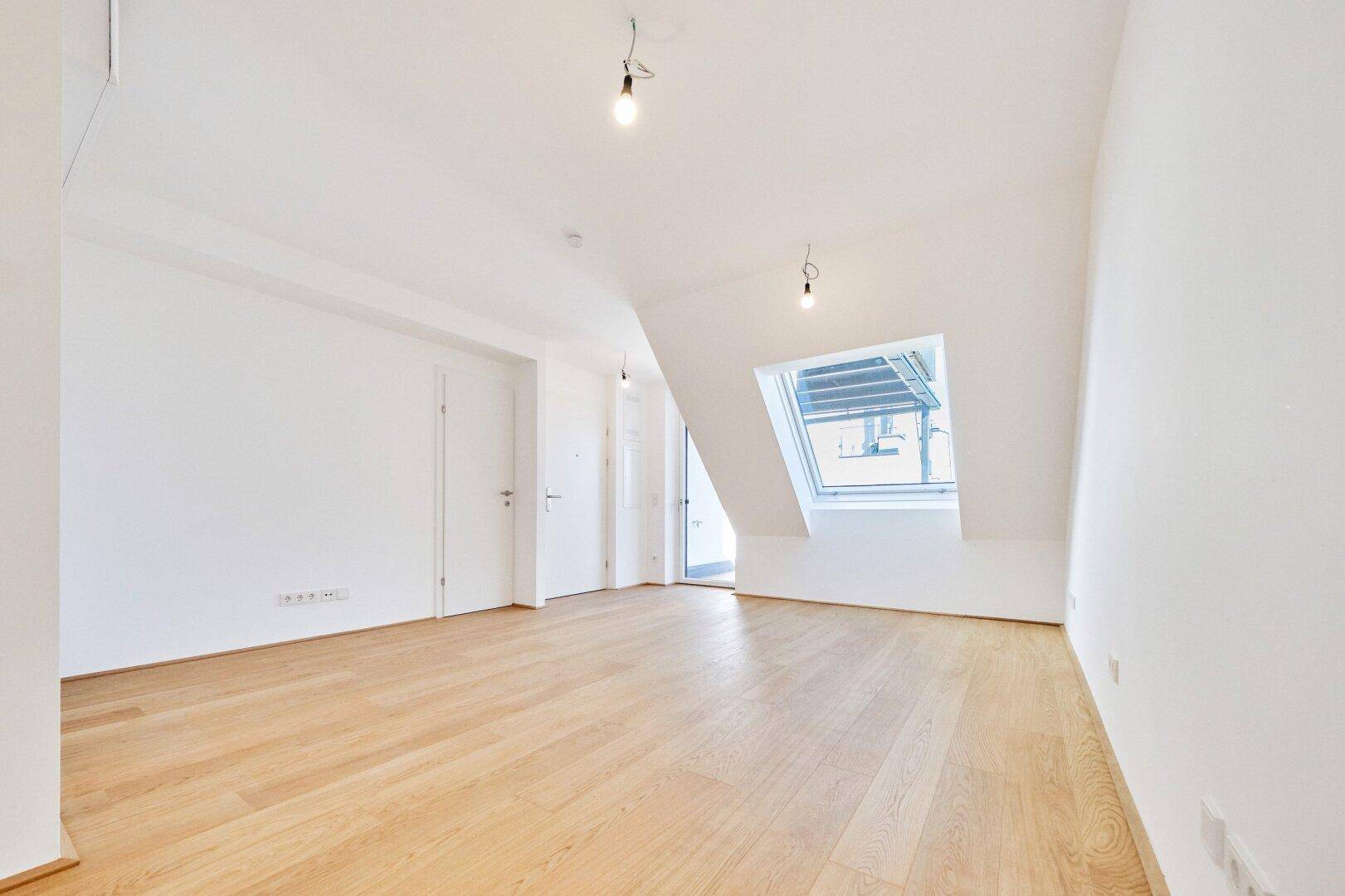 Heller Dachraum mit Holzboden, weißen Wänden und einem großen Dachfenster für viel Licht.