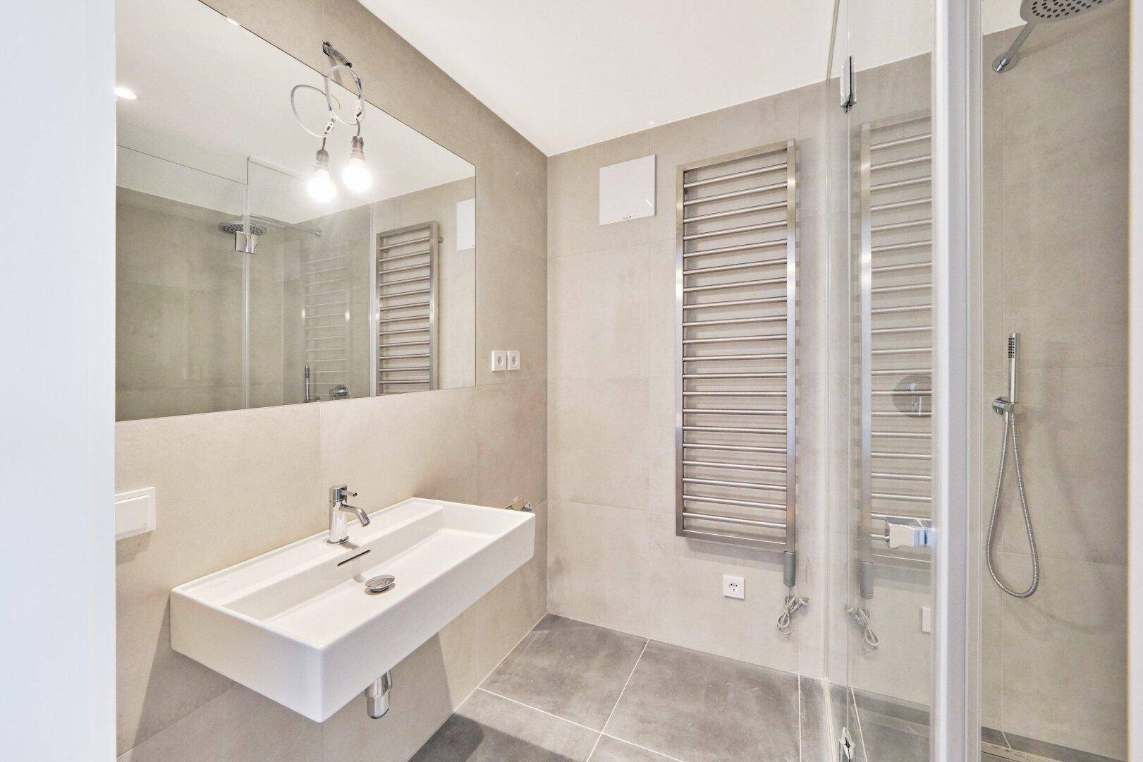 Modernes Badezimmer mit schwebendem Waschbecken, großem Spiegel, Handtuchheizkörper und Duschkabine.