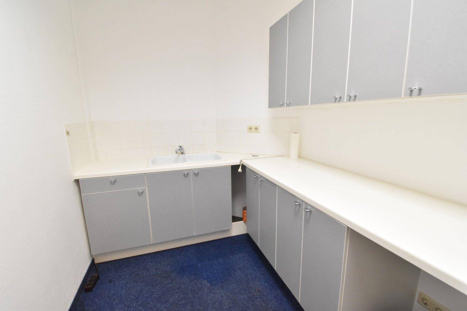 Kleine Küchenzeile mit grauen Schränken, weißer Arbeitsplatte und einem Waschbecken, ideal für Büroräume.