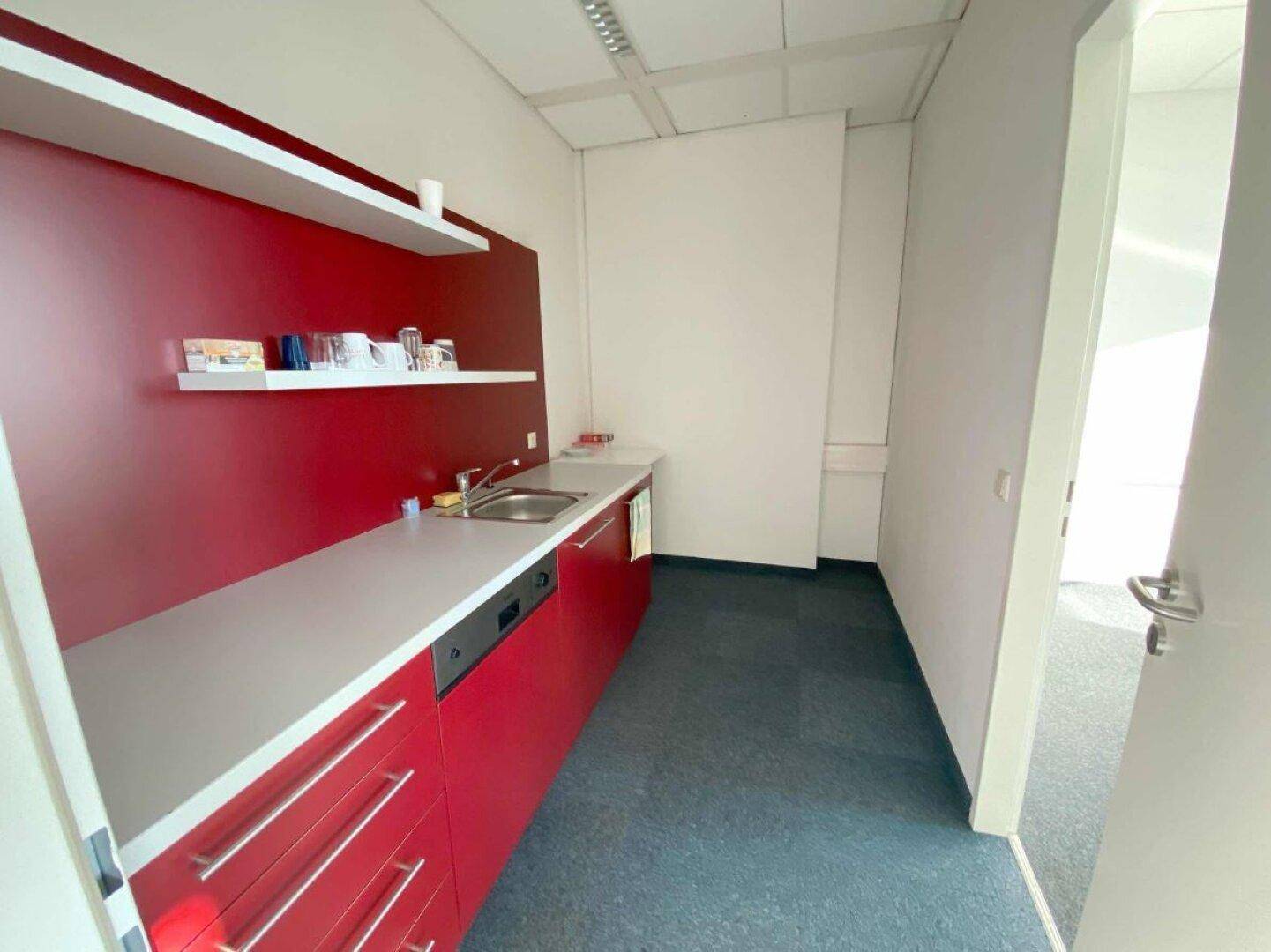 Funktionale Küchenzeile mit roten Schränken, Spüle und Geschirrspüler, ideal für eine Büroumgebung.