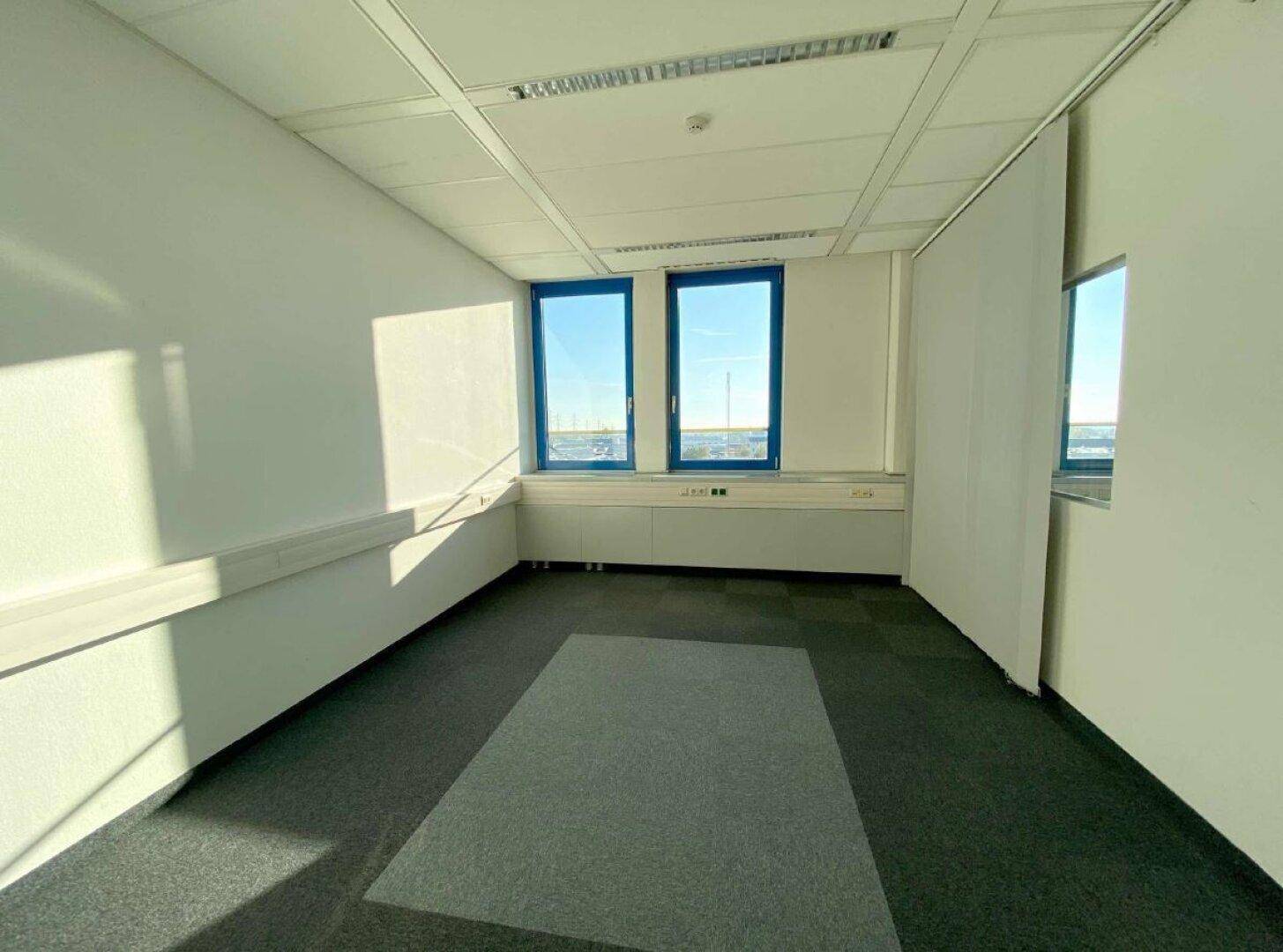 Kleineres Büro mit Teppichboden und zwei Fenstern, die den Raum mit natürlichem Licht versorgen.