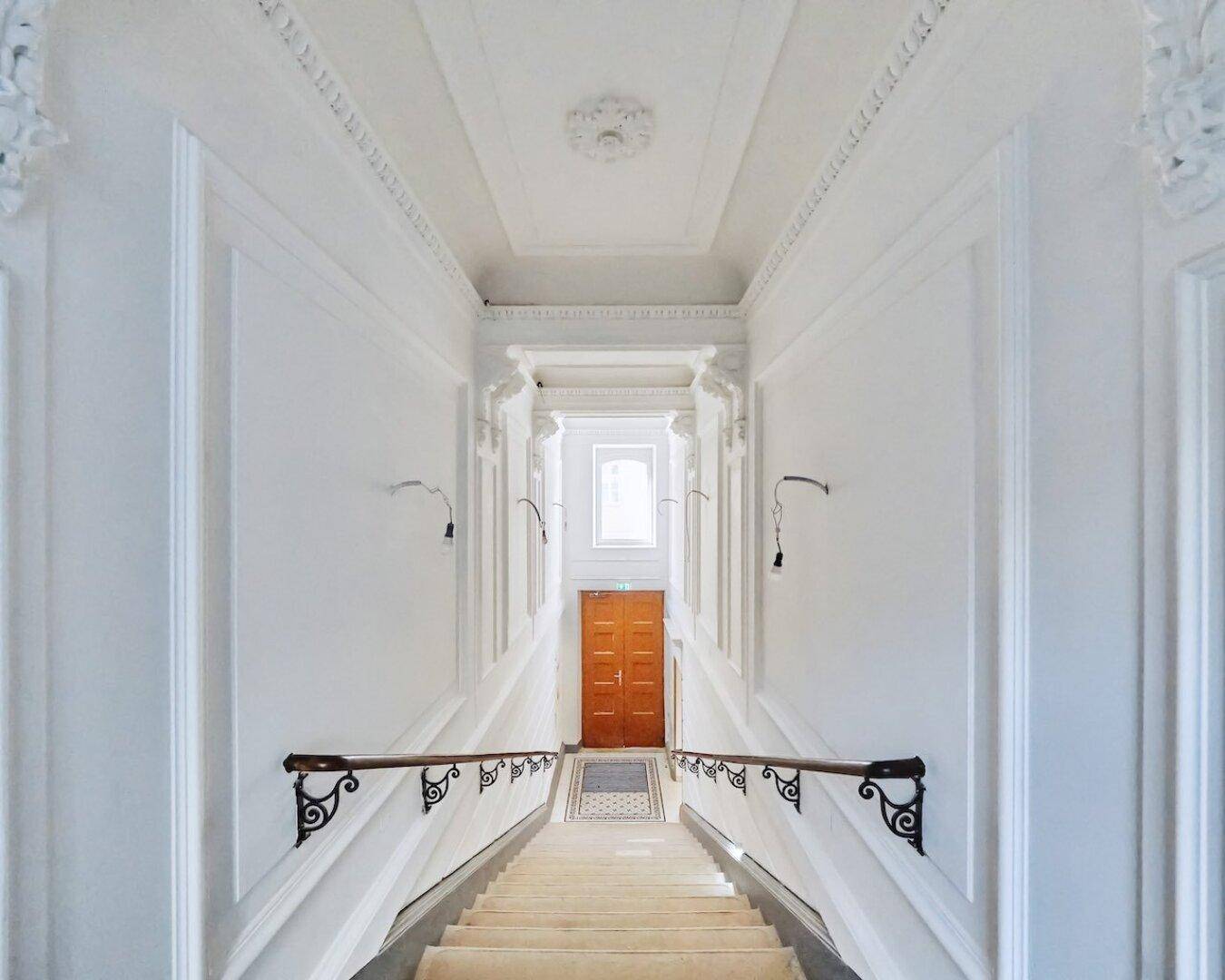 Elegantes Treppenhaus mit weiß gestrichenen Wänden, Stuckelementen und Holzgeländer.