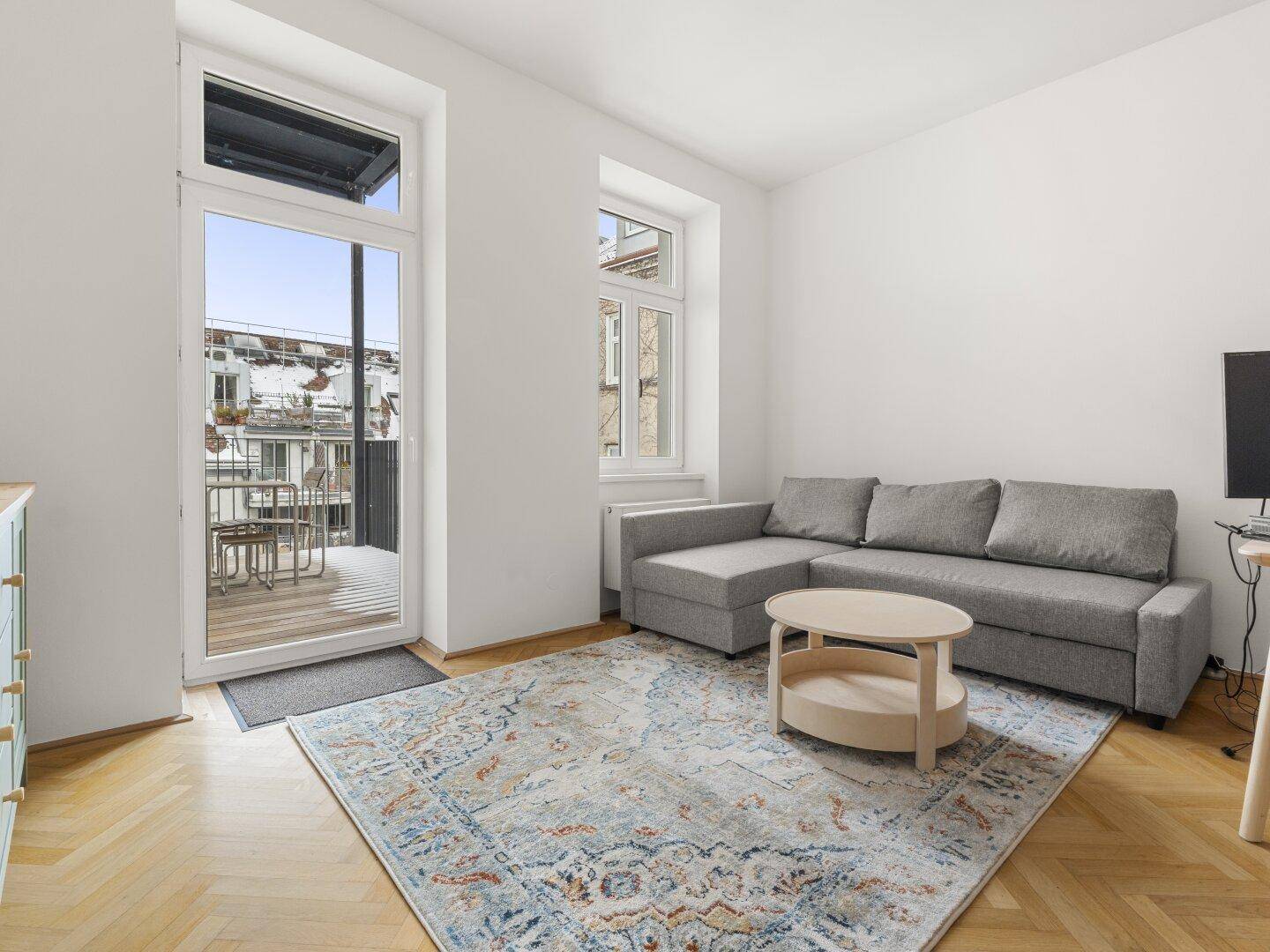 Gemütliches Wohnzimmer mit grauem Sofa, Couchtisch und direktem Zugang zum Balkon.
