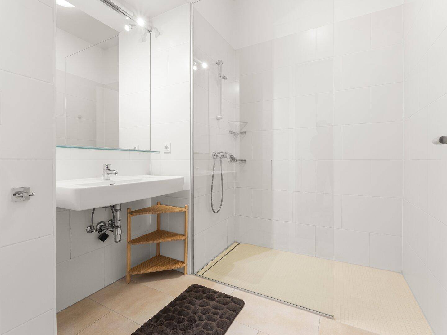 Modernes Badezimmer mit ebenerdiger Dusche, weißem Waschbecken und hellen Fliesen.