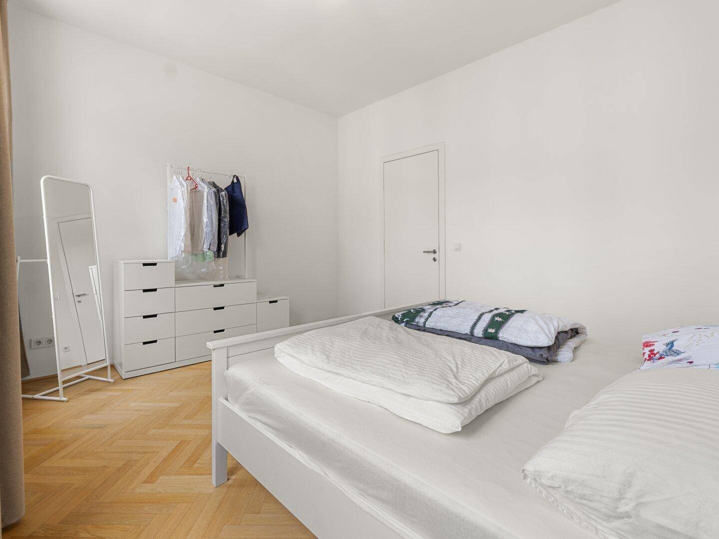 Helles Schlafzimmer mit weißem Bett, Kommode und Kleiderstange, ideal für Stauraum.