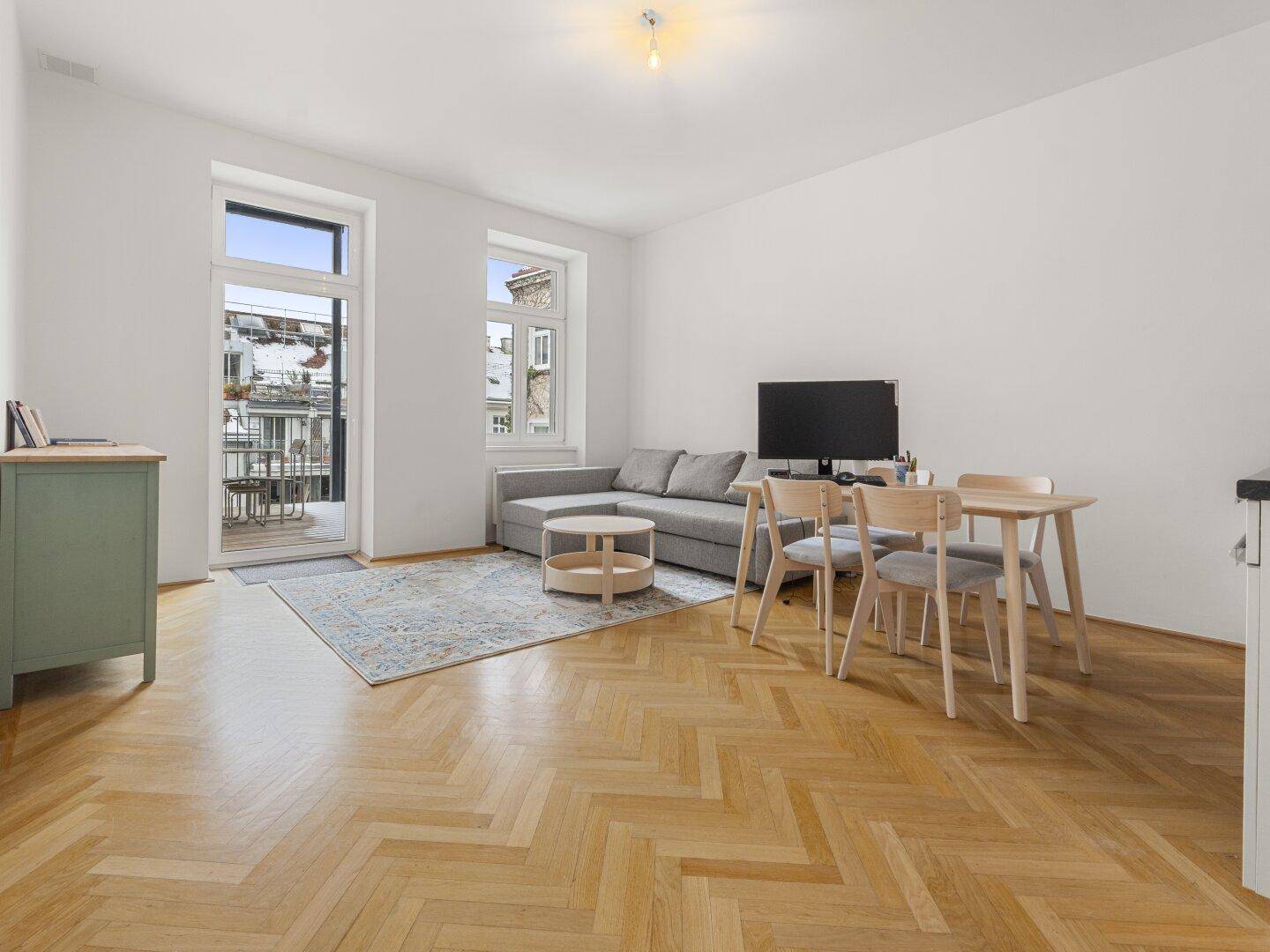 Offener Wohn-Essbereich mit integrierter Küche, Fischgrätparkett und Zugang zum Balkon.