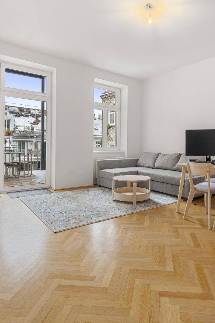 Helles Wohnzimmer mit Fischgrätparkett, gemütlichem Sofa und direktem Zugang zum Balkon.